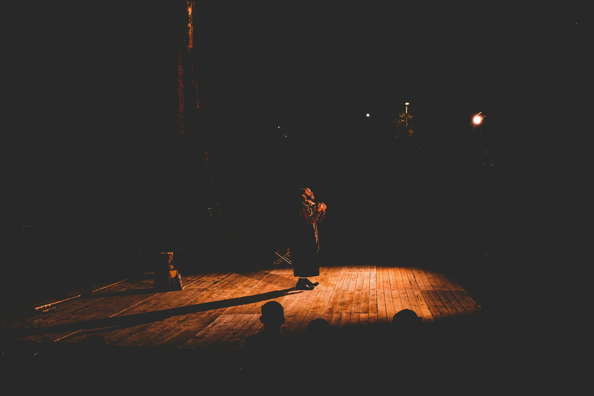 An actor performing on a stage in front of dark audience with stage lights illuminating them.