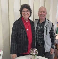 A woman and a man smiling and standing close together indoors.