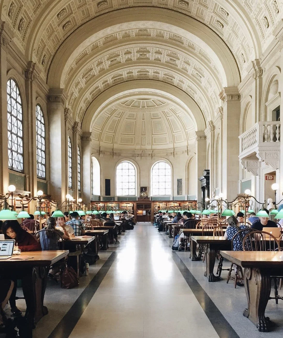 People studying at a library reading room with tables, books, and laptops.