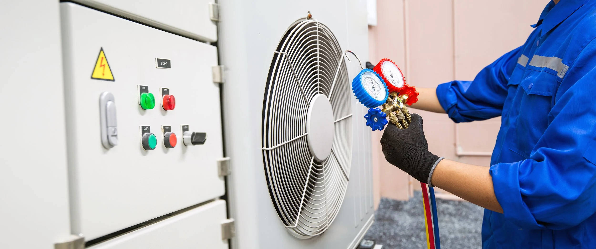 Technician wearing black gloves and blue uniform using manifold gauge set on an industrial HVAC system.