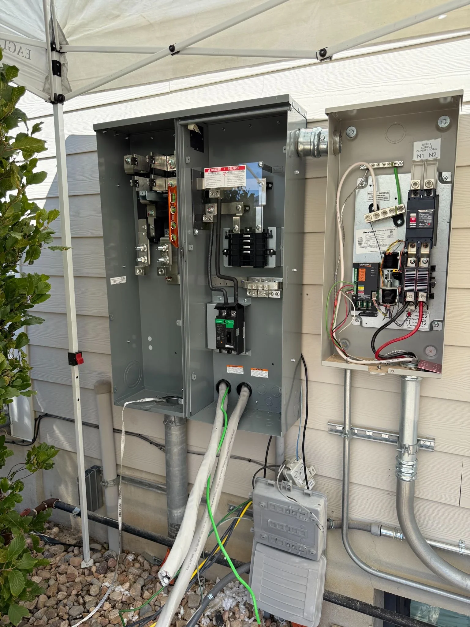 Open outdoor electrical service boxes and generator transfer switch mounted on a house wall.