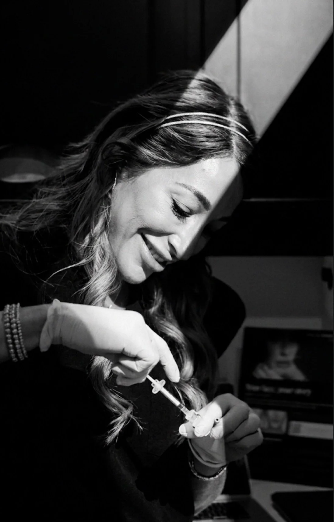 A woman smiling as she prepares to receive a vaccination shot, with a syringe in her hand.