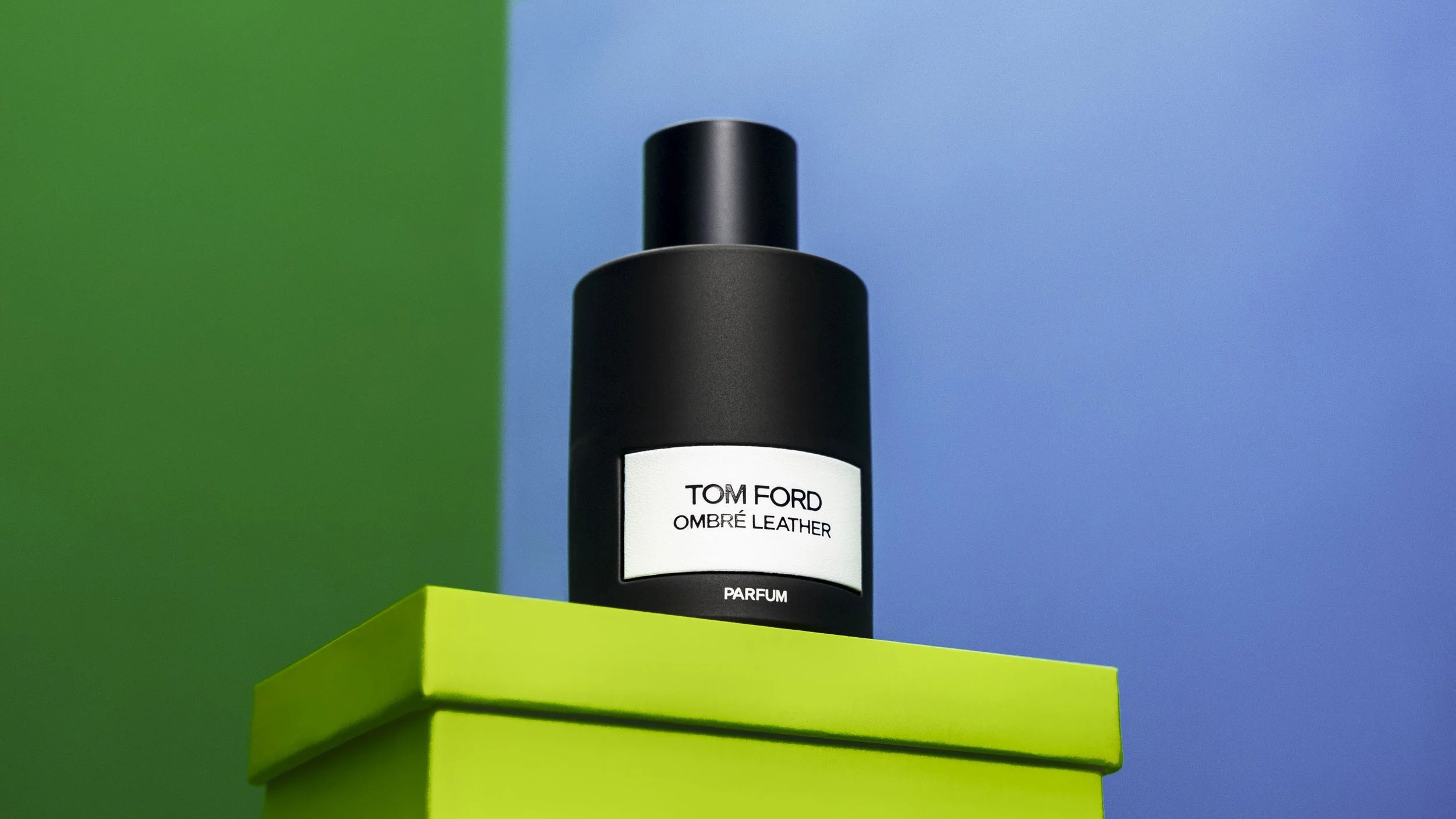 A bottle of Tom Ford Ombre Leather perfume on a bright yellow-green surface against a background with green and blue sections.