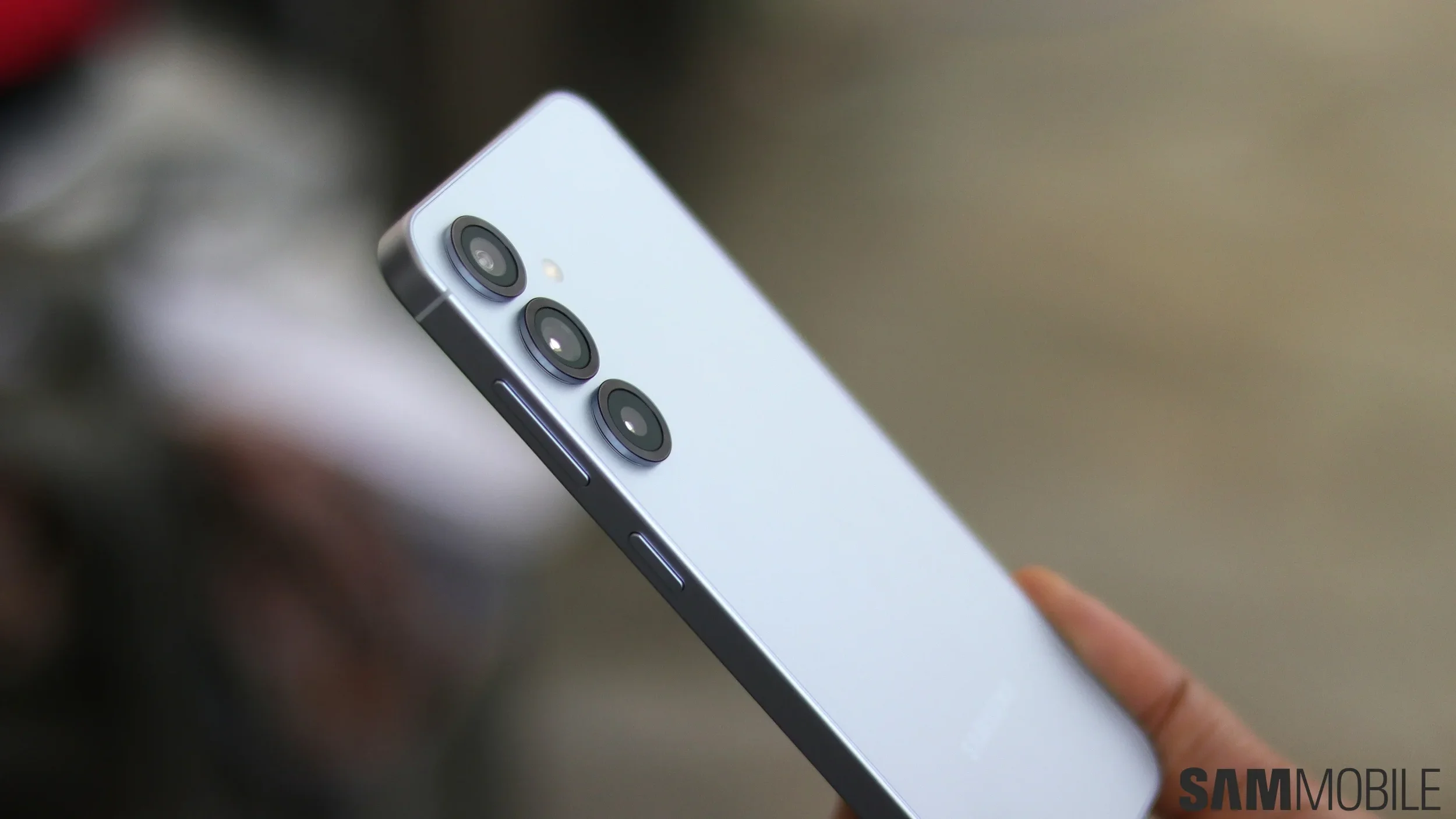 Close-up of a modern smartphone with three camera lenses on the back and a person's finger touching the side of the device.