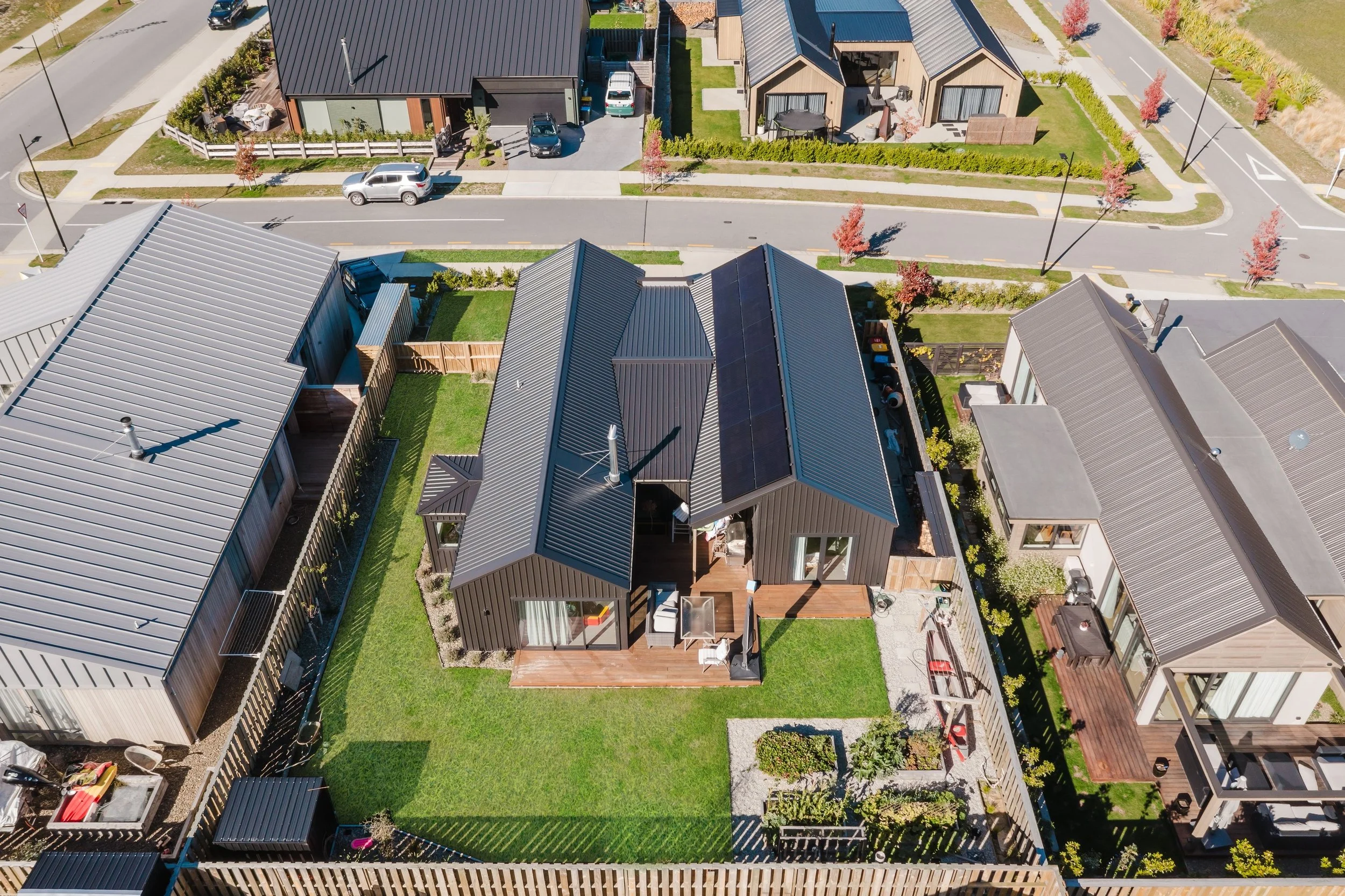 Aerial view of modern houses with metal roofs, small yards, and landscaped gardens in a suburban neighborhood.