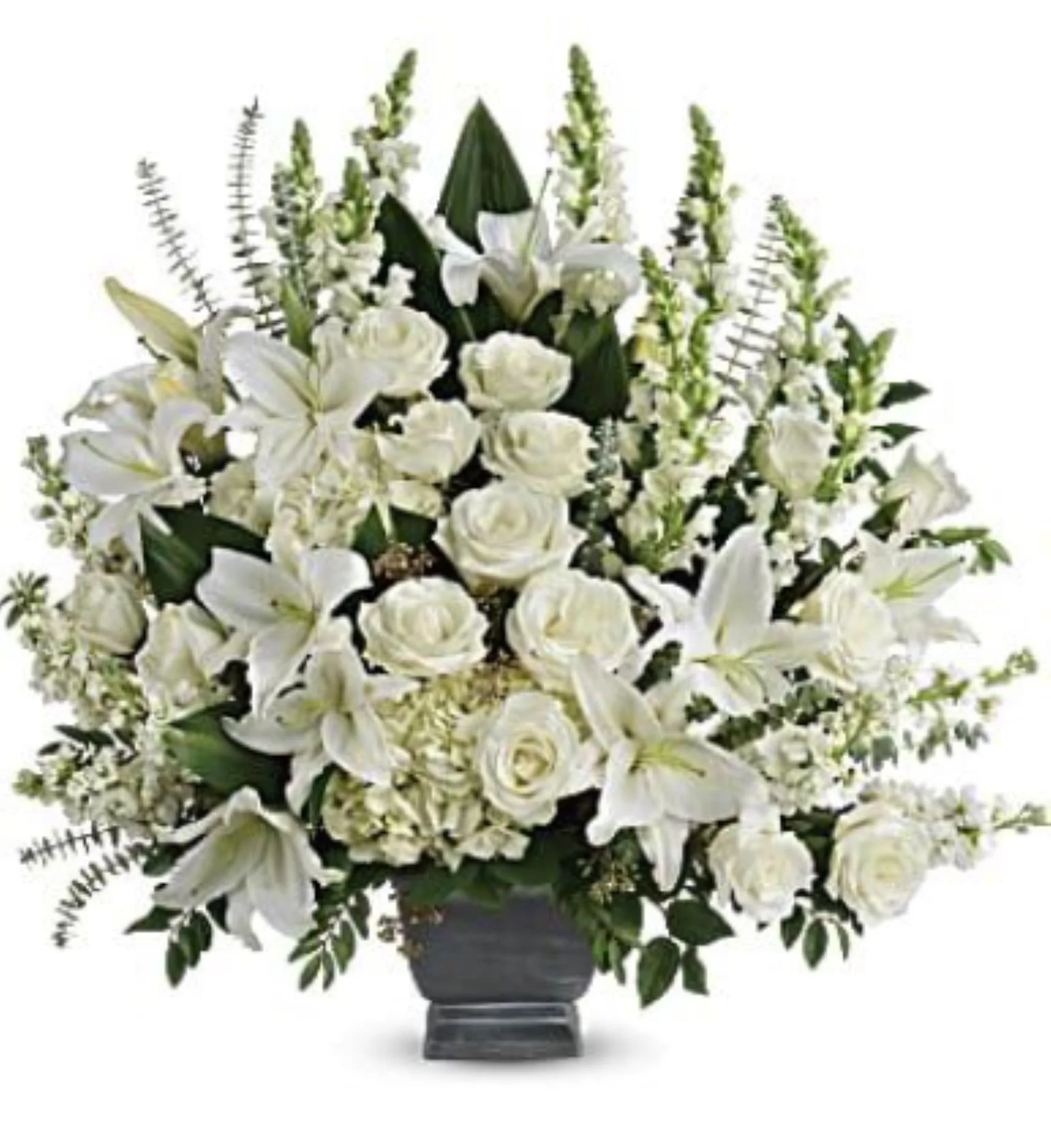 One sized white funeral arrangement with roses, lilies and snap dragons