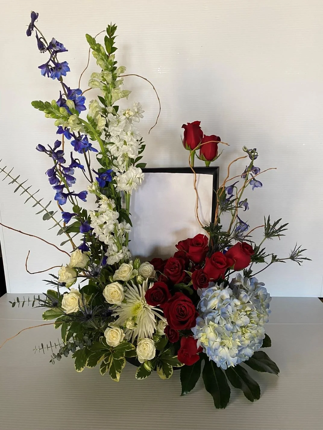 Red, white & blue flowers surround deceased photo
