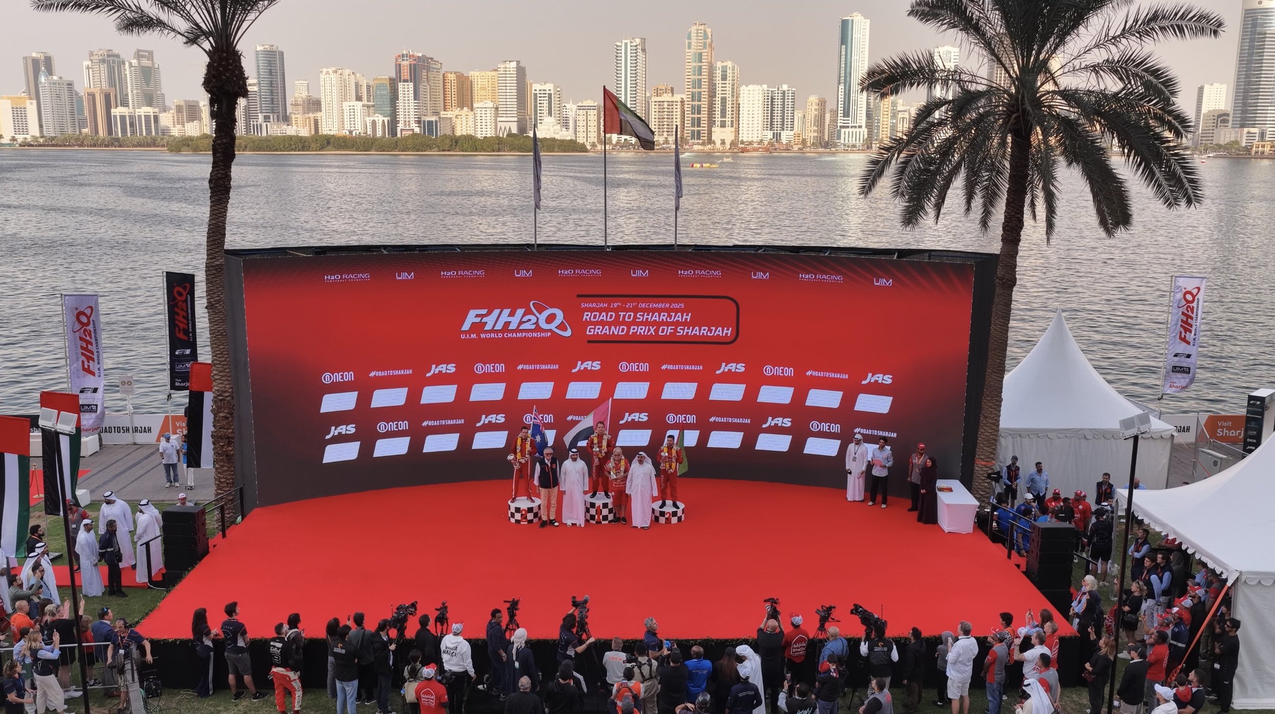 Speedboat racing on a body of water with a logo saying FIH2Q in the foreground and two other speedboats trailing behind.