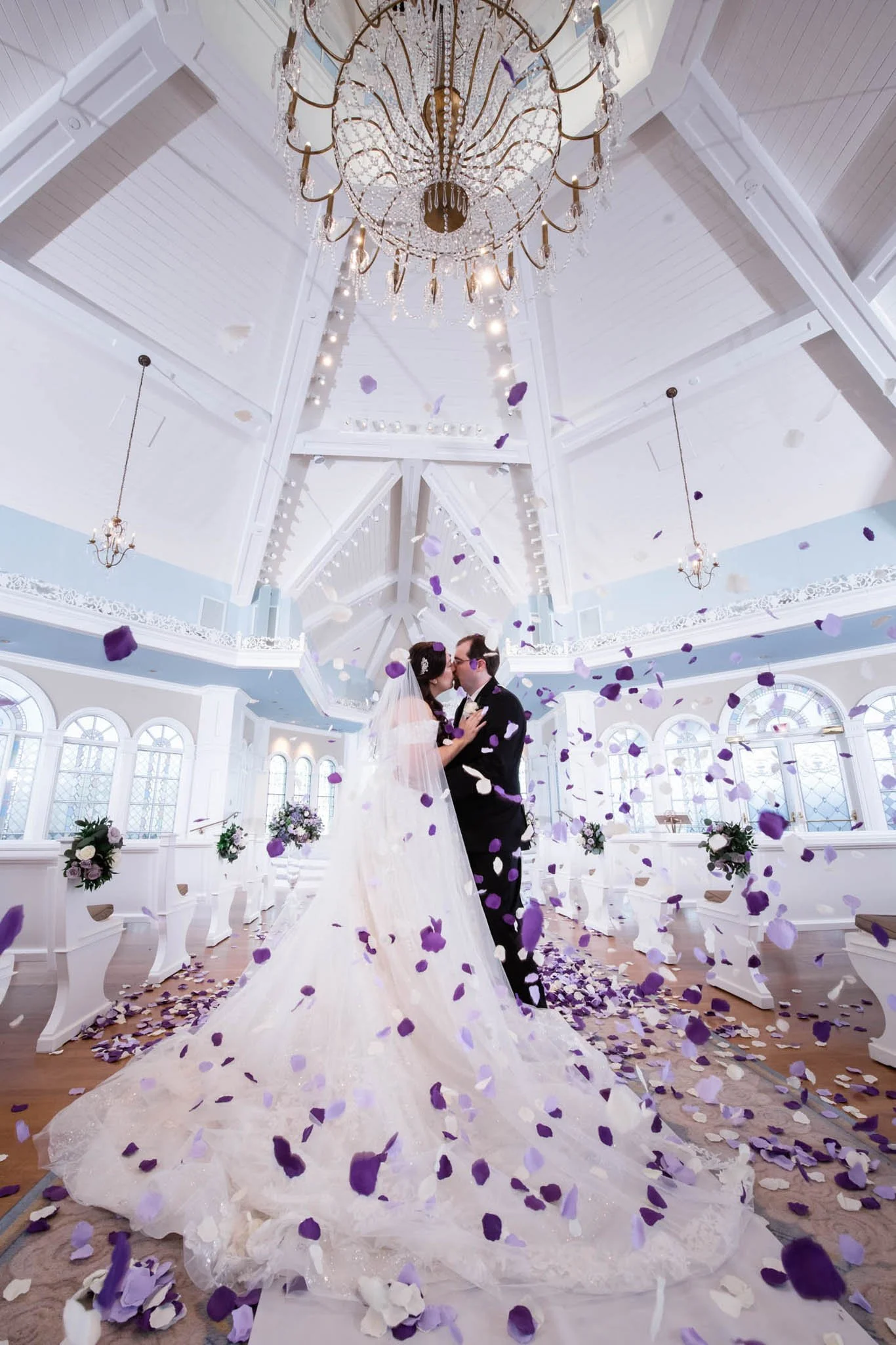 A bride and groom kissing inside Disney's Wedding Pavilion with falling purple and white confetti.