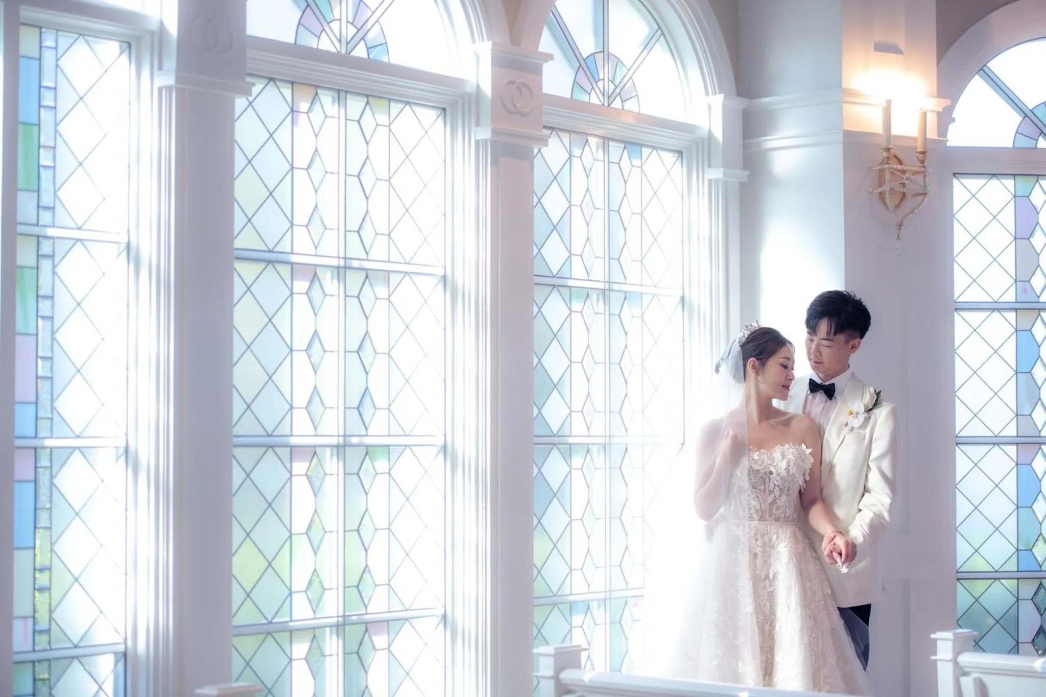 A bride and groom holding hands inside Disney's Wedding Pavilion with large stained glass windows.