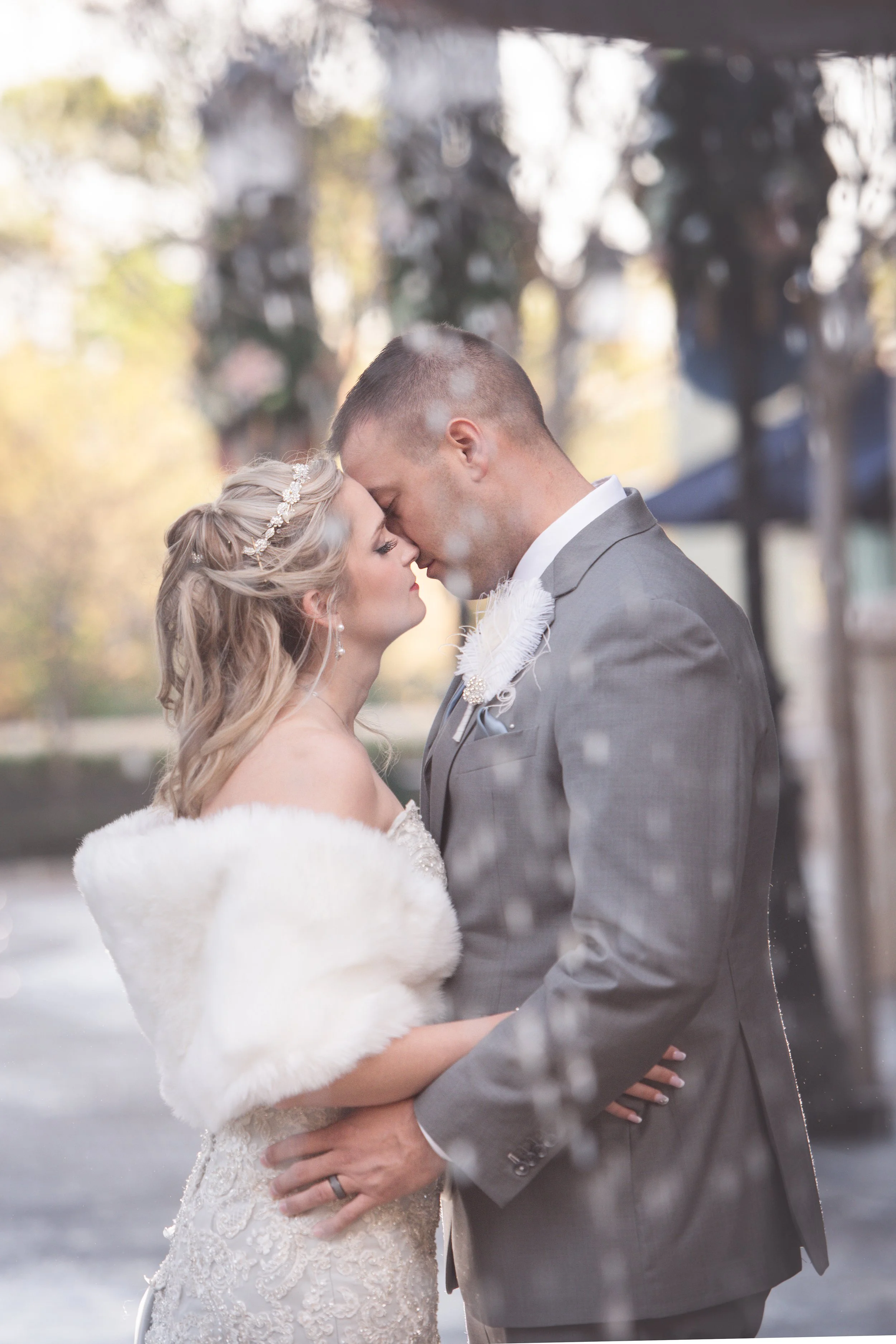 A bride and groom share an intimate moment, touching foreheads, outside on their wedding day.