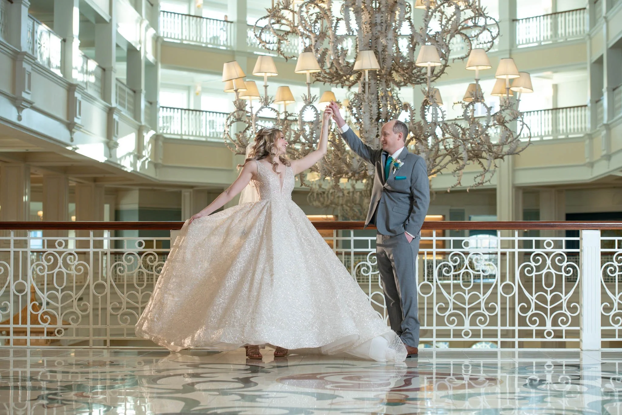 A bride and groom dancing in an elegant hotel lobby with a large chandelier in the background.