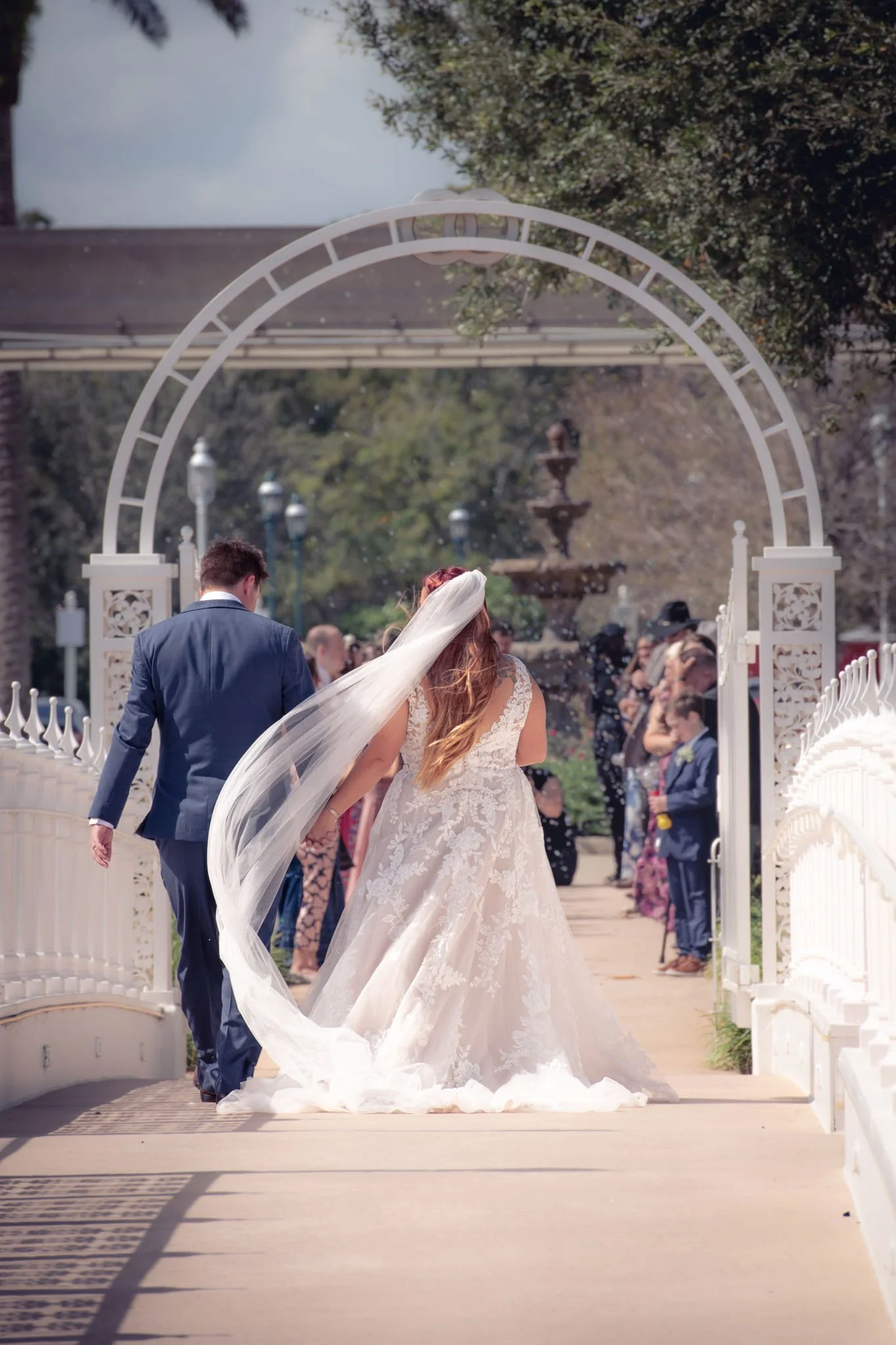 Bride and groom walking under an archway at Disney Wedding Pavilion during their wedding ceremony, with guests in the background.