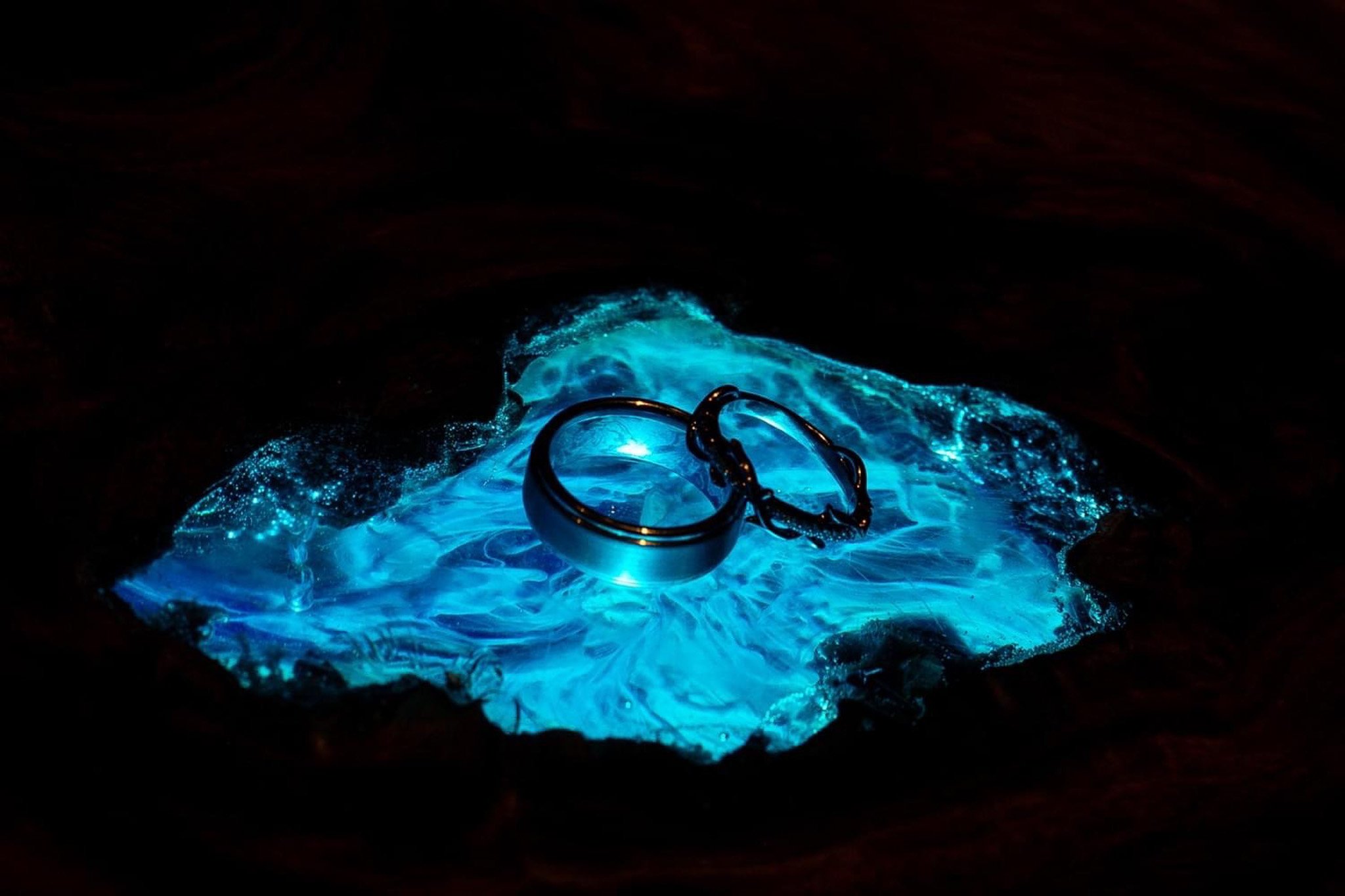 A glowing blue surface of a substance, with silver rings placed on top of it, illuminated in the dark.