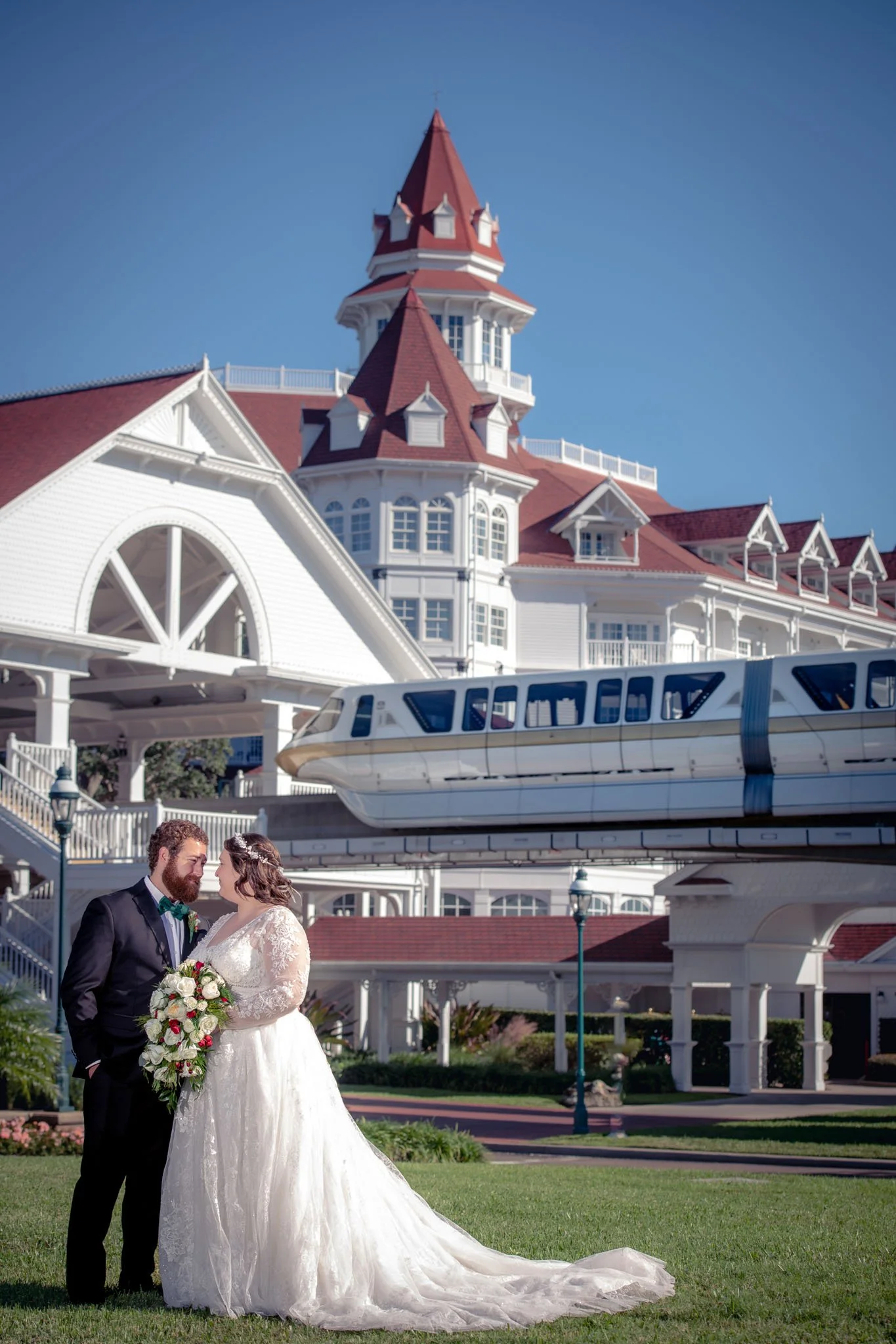 A bride and groom outside Disneyland's Grand Floridian hotel with the monorail passing overhead.