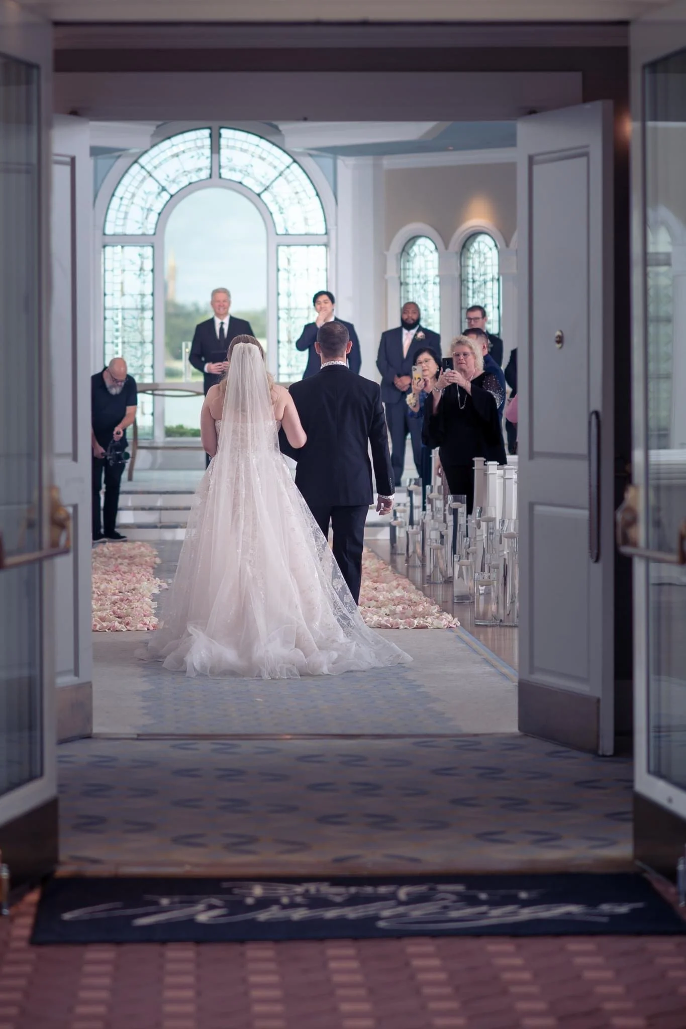 Bride and groom walking down the aisle in a wedding ceremony, with guests taking photos and watching indoors.