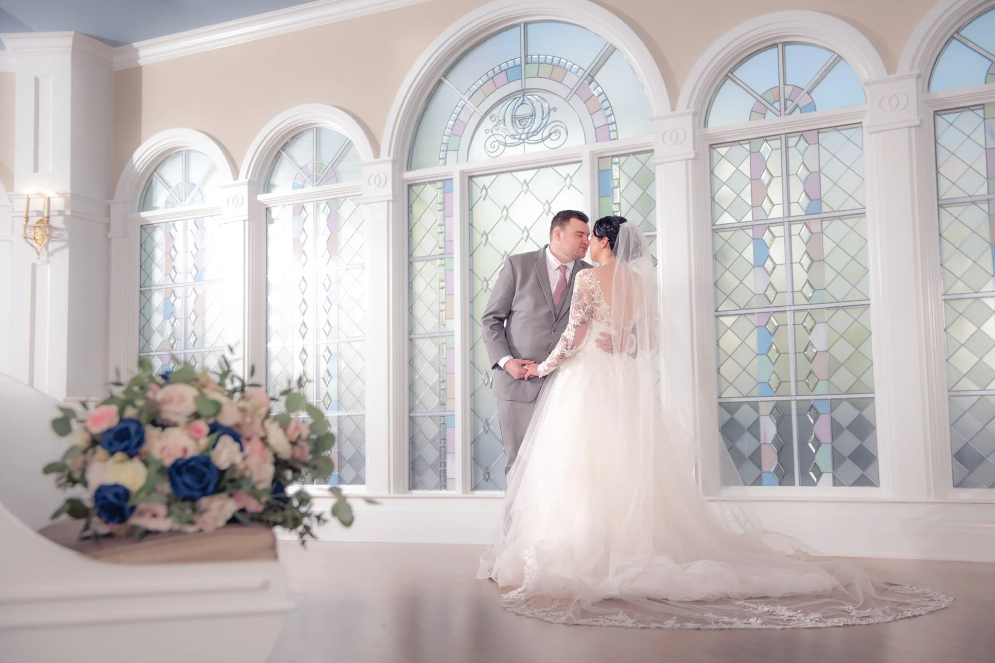 A bride and groom standing close together, about to kiss, in a bright room with large stained glass windows at Disney's Wedding Pavlion.