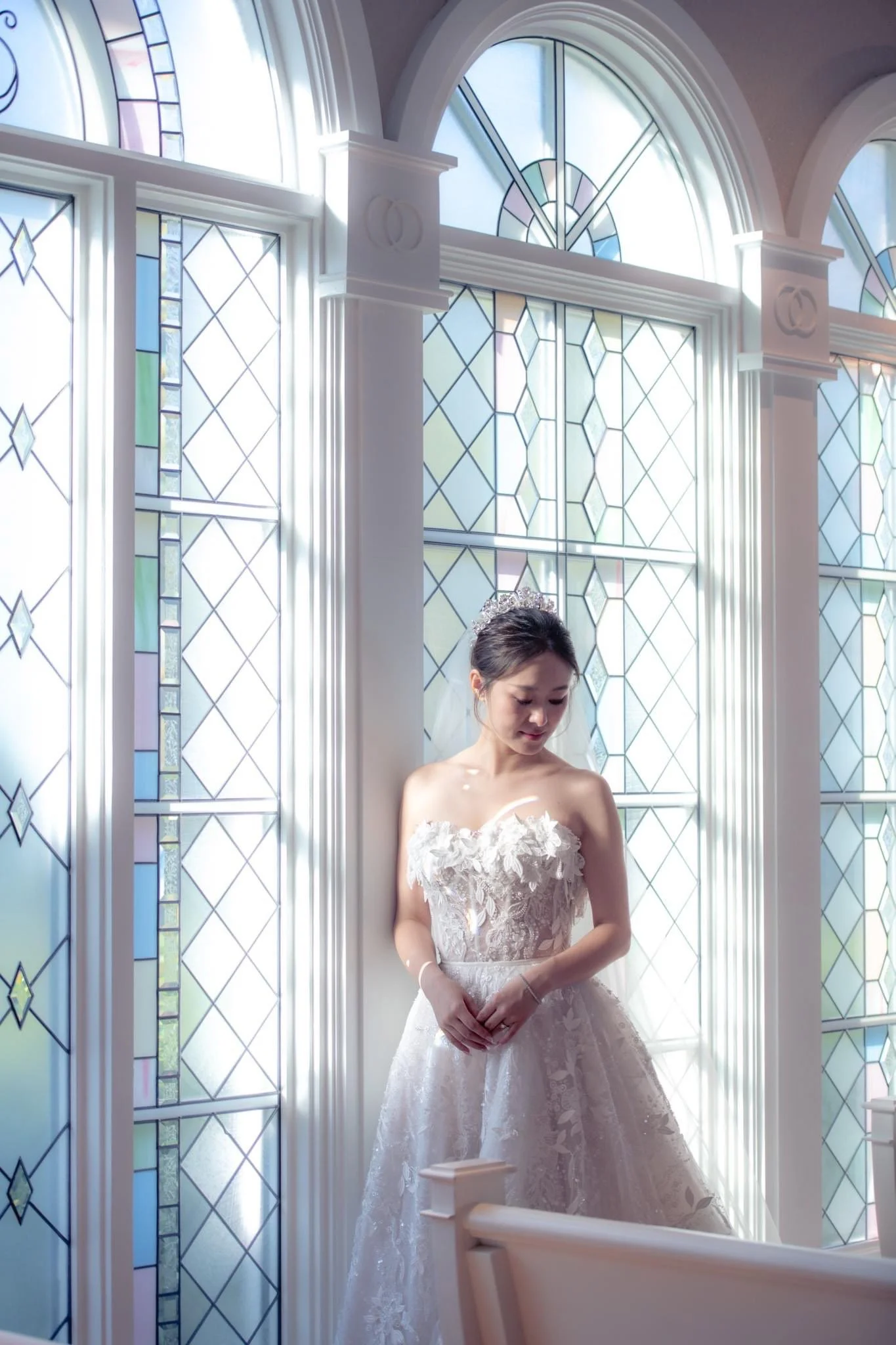A bride standing inside Disney's Wedding Pavilion with stained glass windows, wearing a white wedding gown and a tiara.