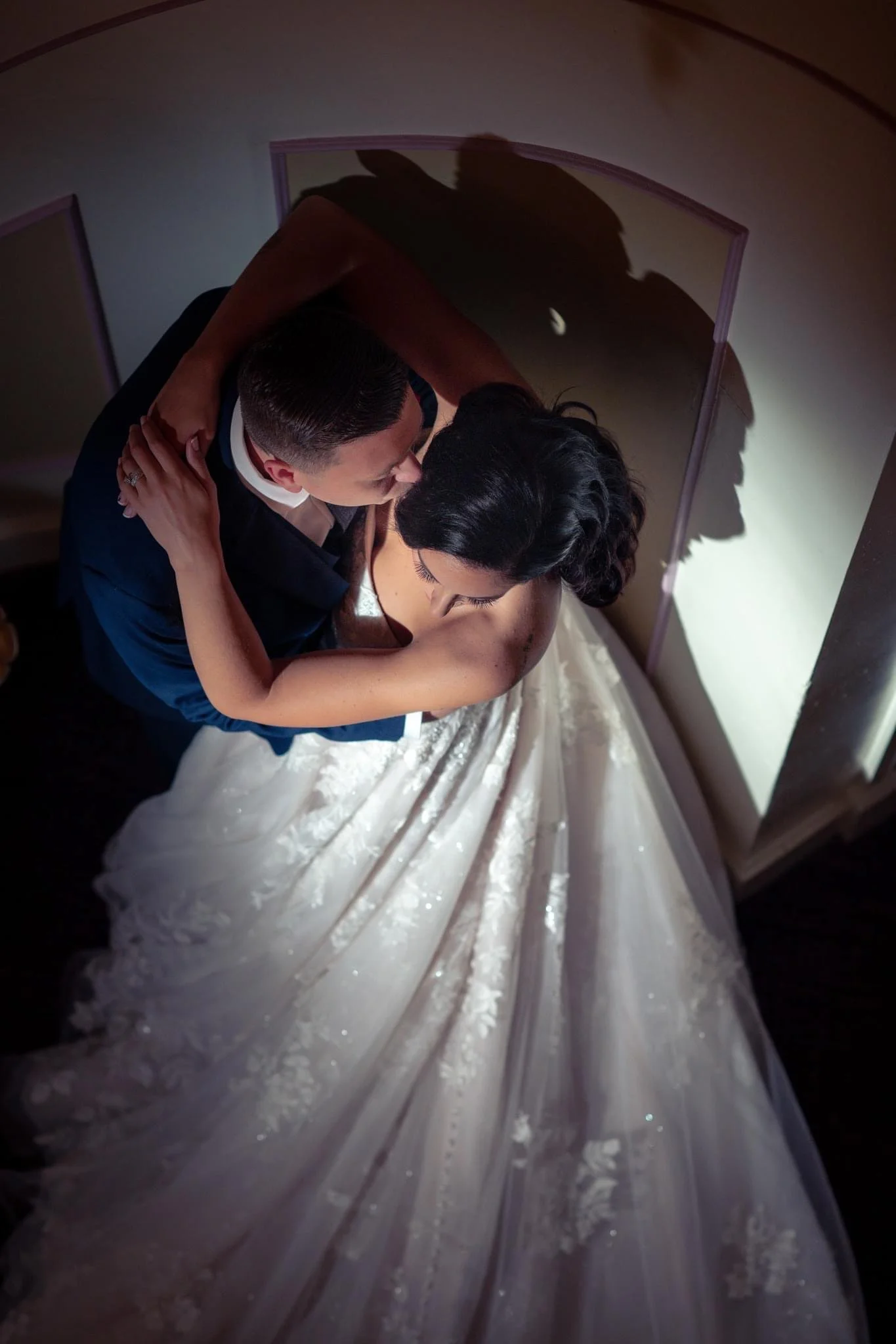 A bride and groom sharing a kiss indoors, with their shadows cast on the wall behind them.