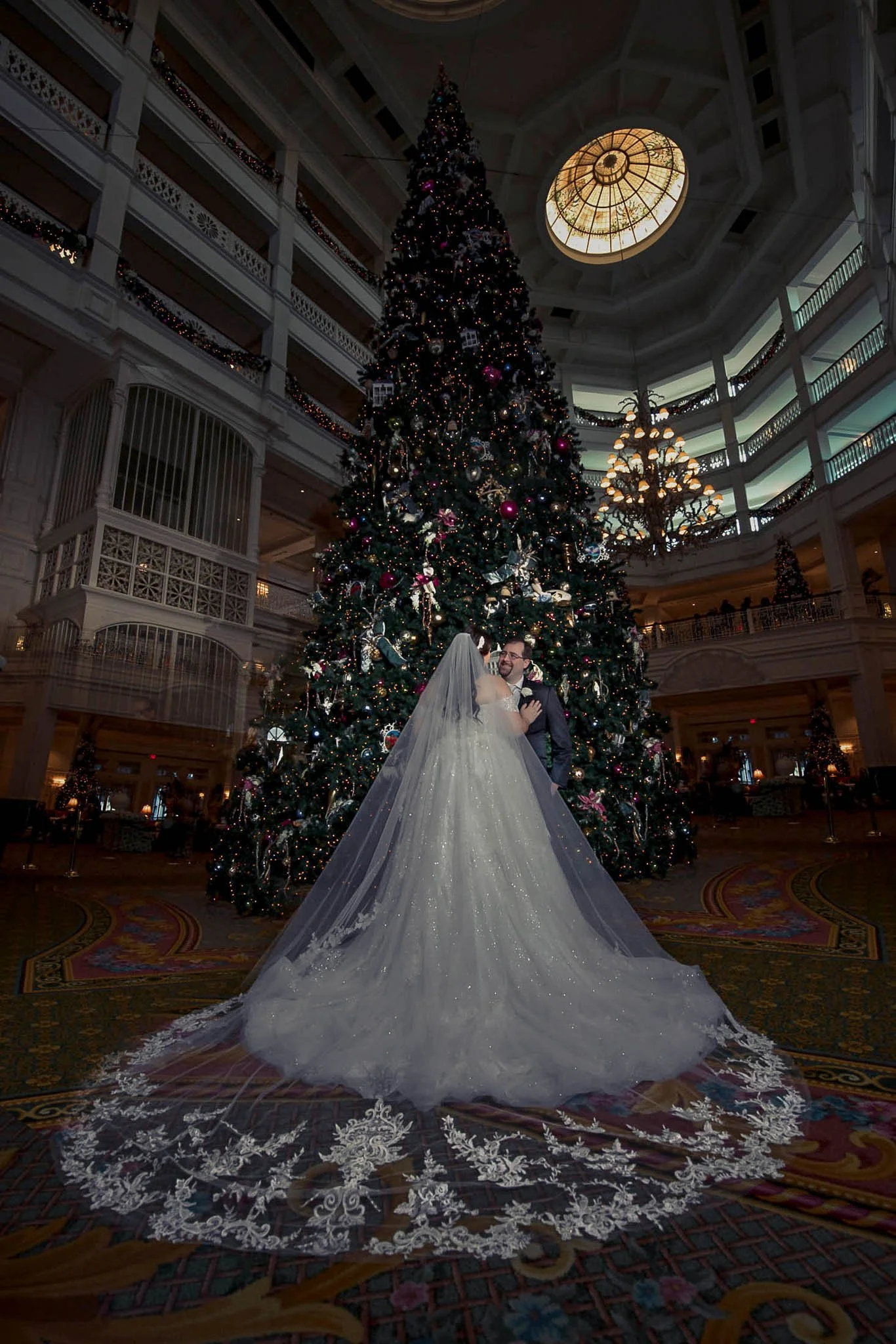 Bride and groom sharing a dance in front of a decorated Christmas tree inside a grand hotel lobby.