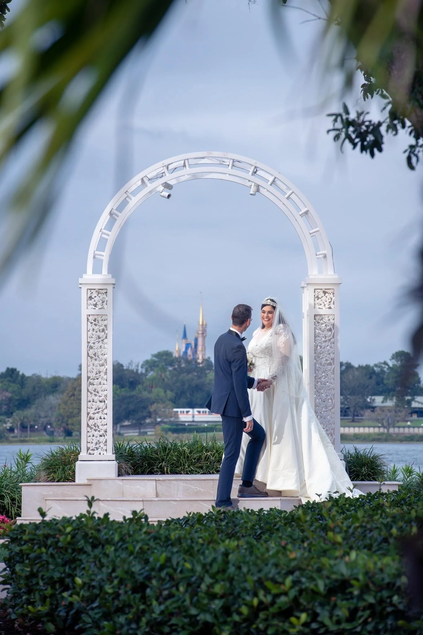 Bride and groom holding hands at Disney's Wedding Pavilion / Picture Point, with a castle in the background.