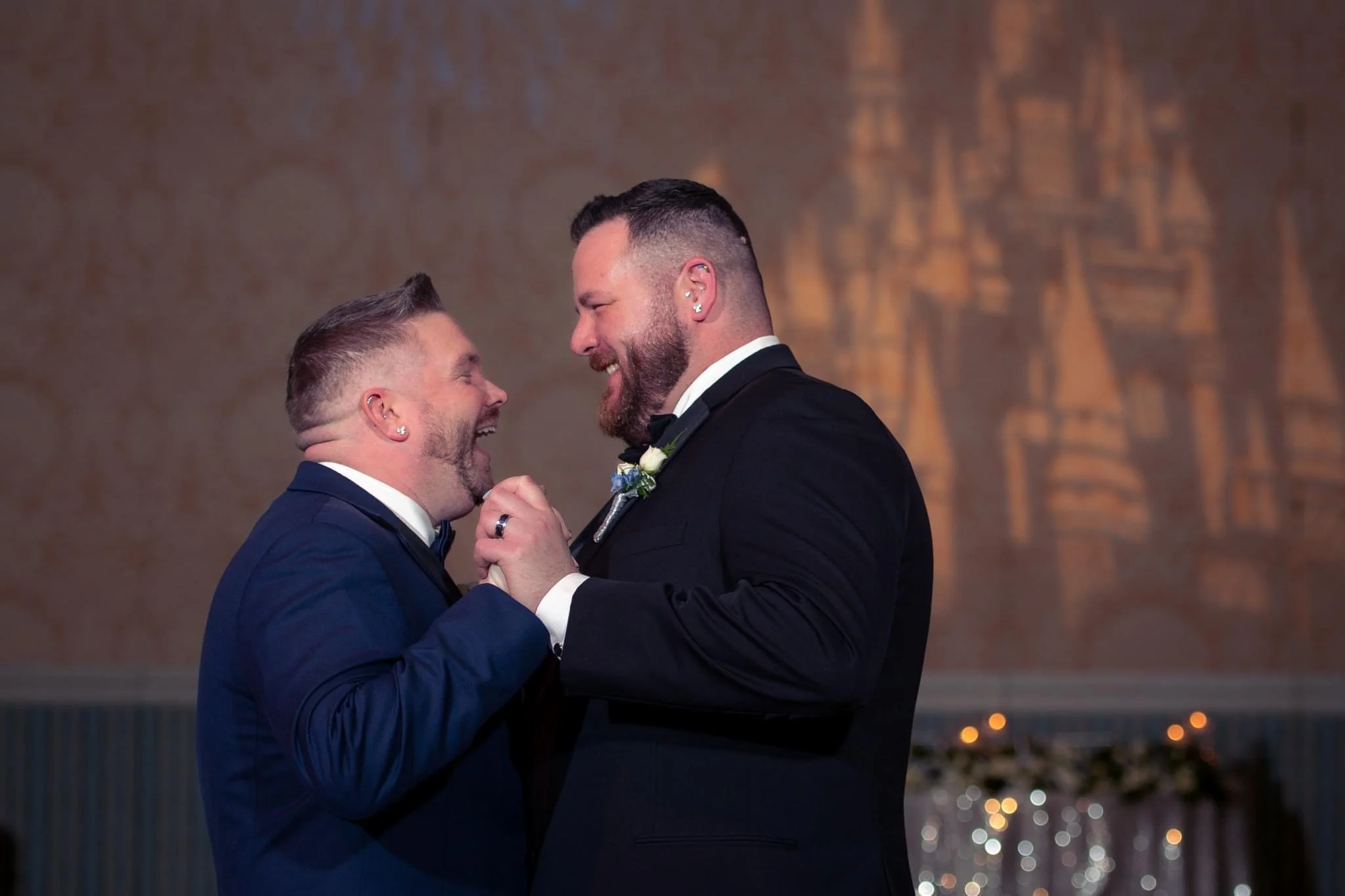 Two men in tuxedos sharing a joyful moment and holding hands during a Disney wedding ceremony.