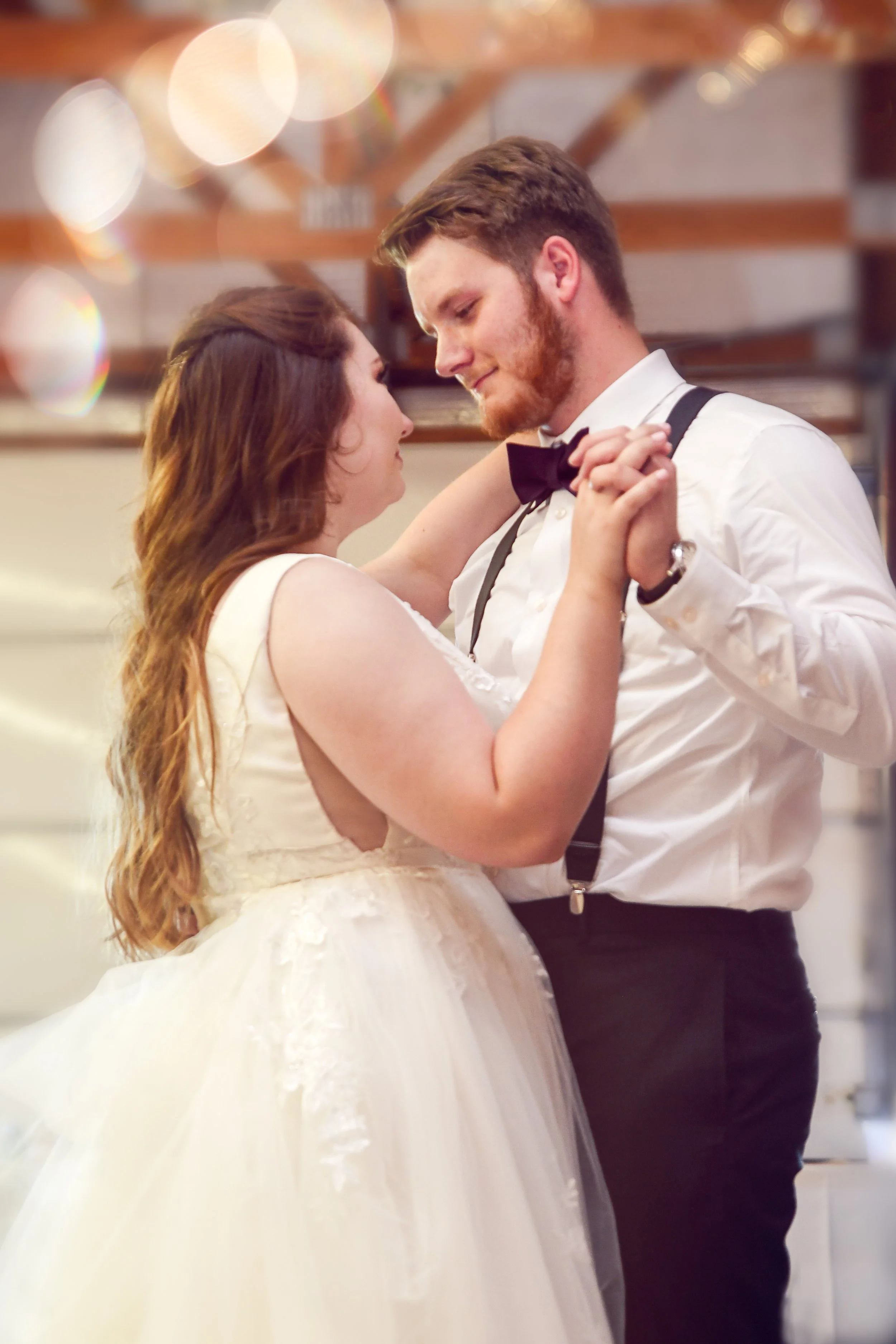 A couple dancing, the woman in a wedding dress and the man in a tuxedo, sharing a romantic moment at their wedding reception.