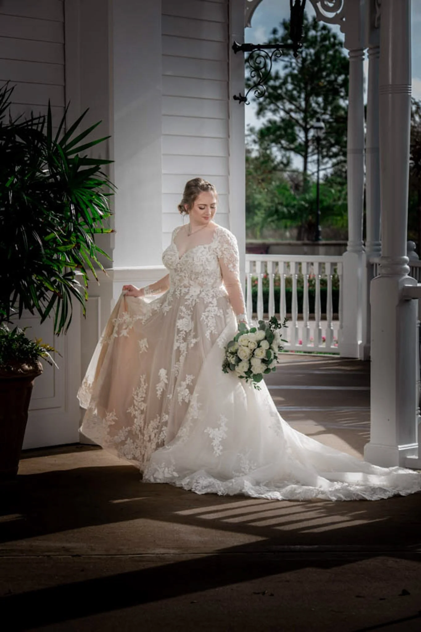 Bride in a lace wedding dress holding a bouquet, standing on a porch at the Grand Floridian 