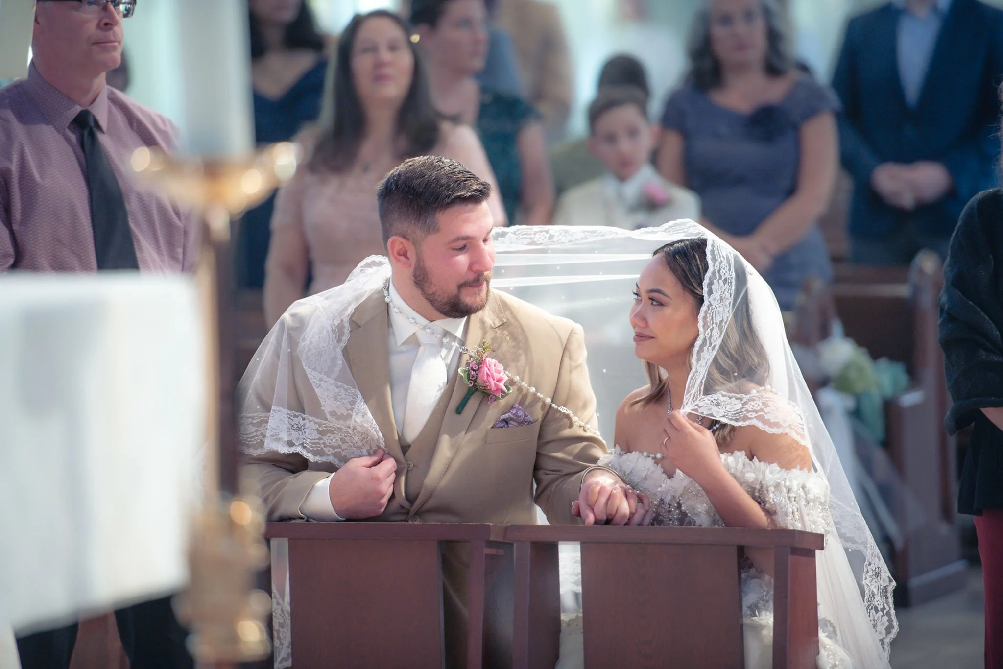 A bride and groom sitting at the altar during their wedding ceremony, holding hands and gazing at each other, with guests seated behind them.