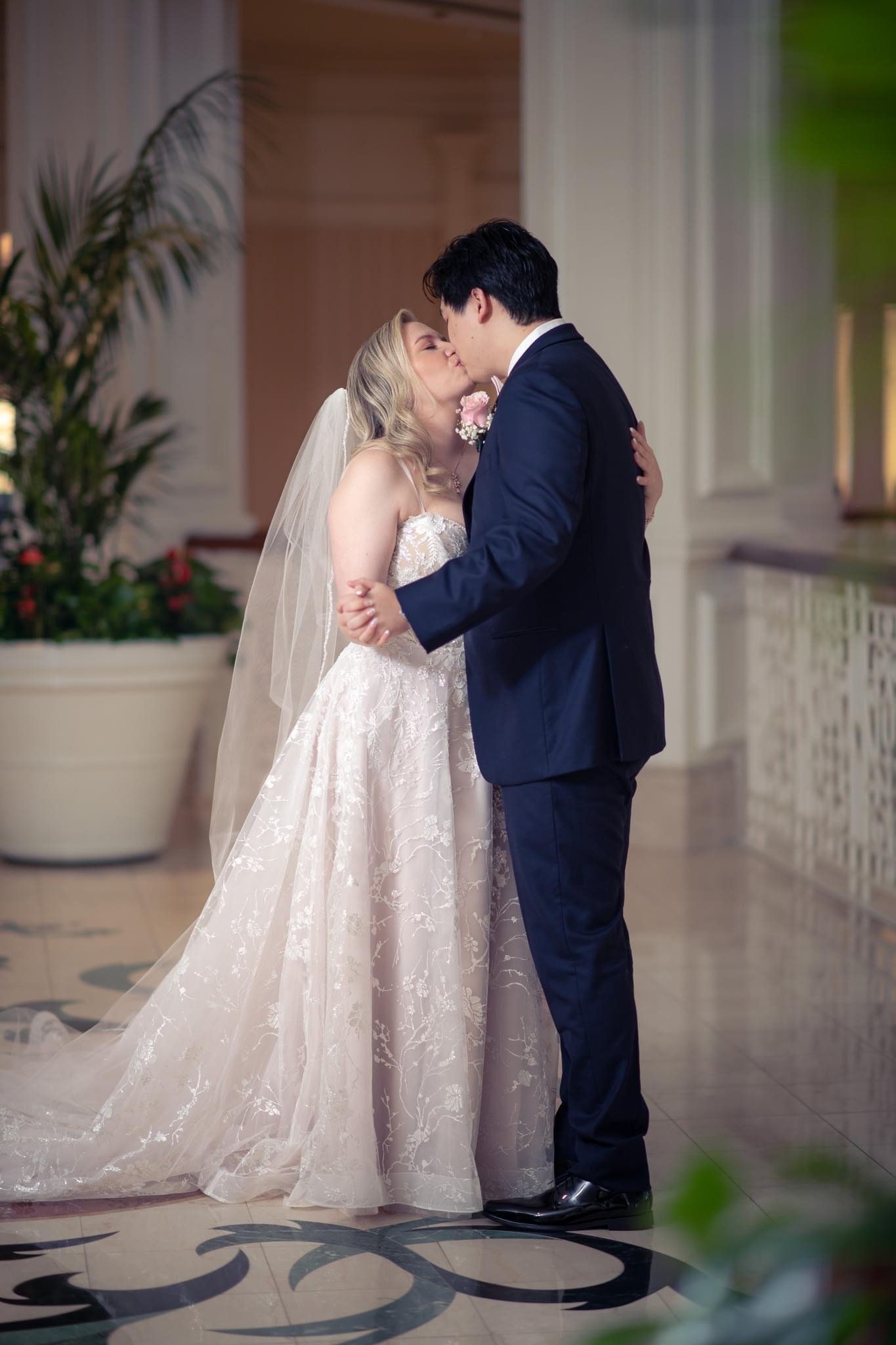 A bride and groom sharing a kiss during their wedding, with the bride in a white gown and veil, and the groom in a dark suit.