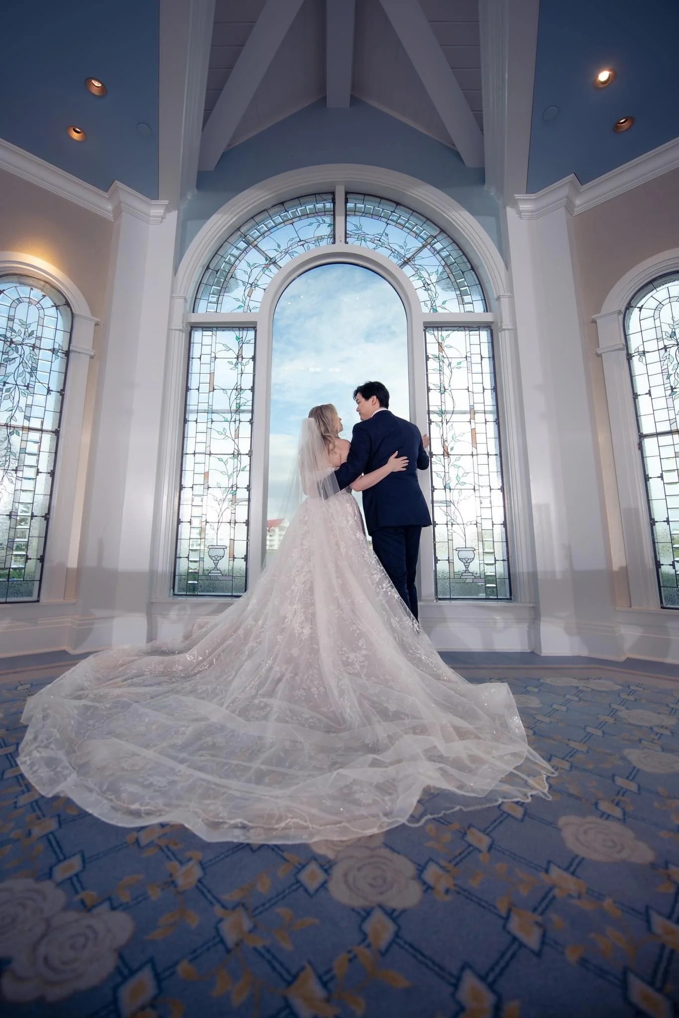 Bride and groom standing inside a church near large stained glass windows at Disney's Wedding Pavilion, gazing at each other.