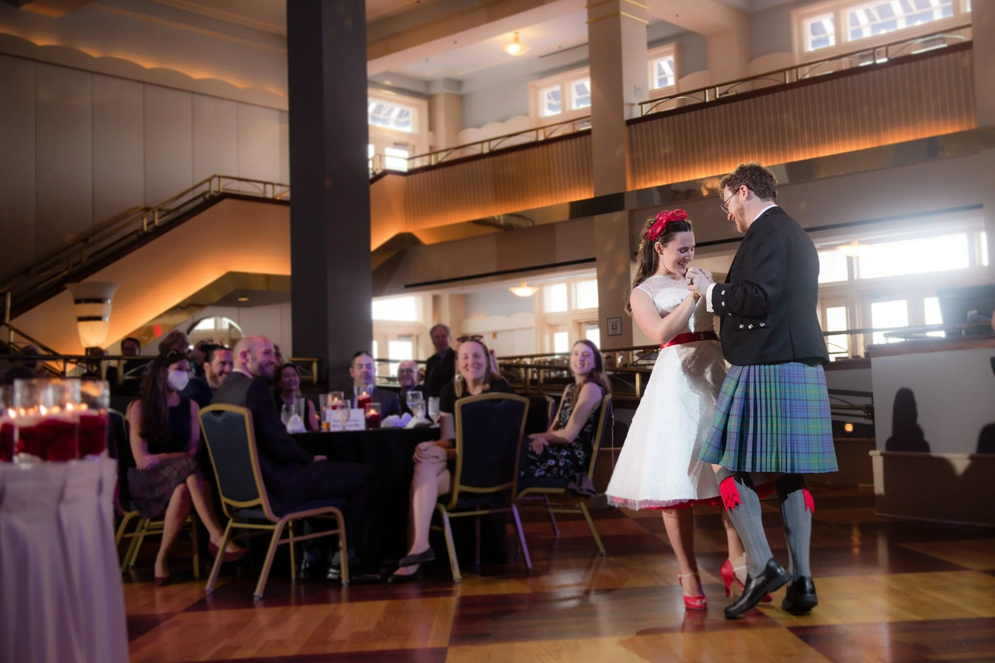 A bride and groom sharing a dance at their wedding reception, with guests seated at tables watching and smiling.