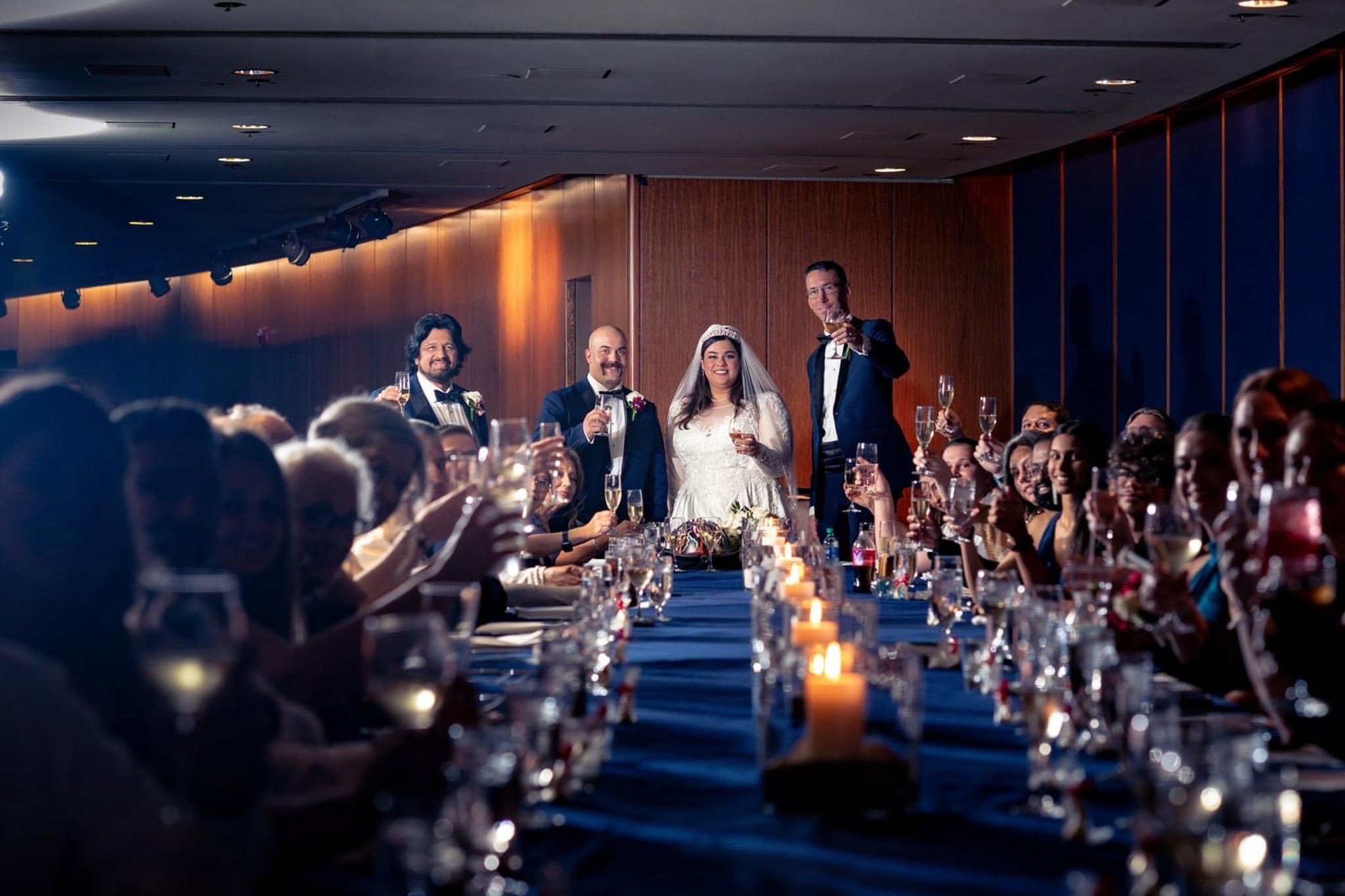 Group of wedding guests raising glasses during a toast at a banquet hall.