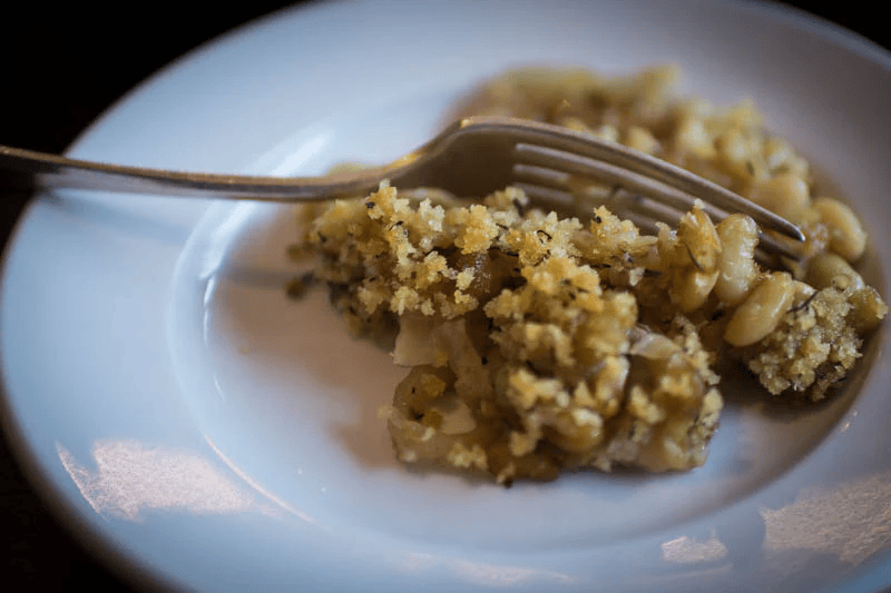 A white plate with a fork and a serving of macaroni and cheese topped with breadcrumbs.