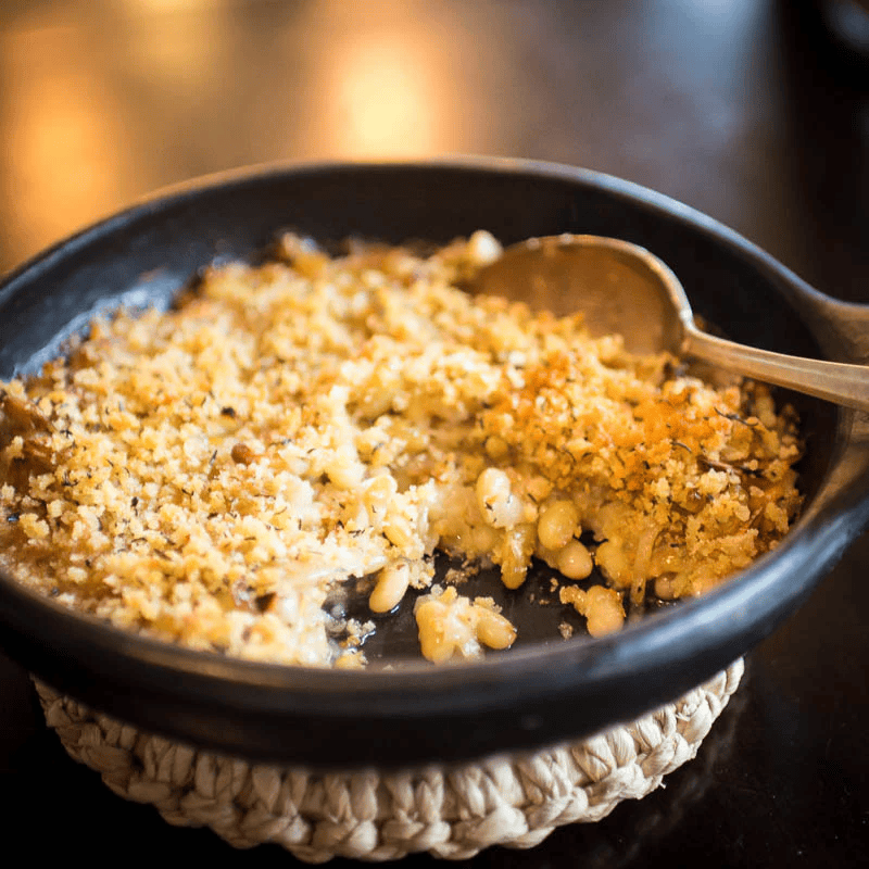 Baked macaroni and cheese with a breadcrumb topping in a dark bowl, with a spoon placed inside.