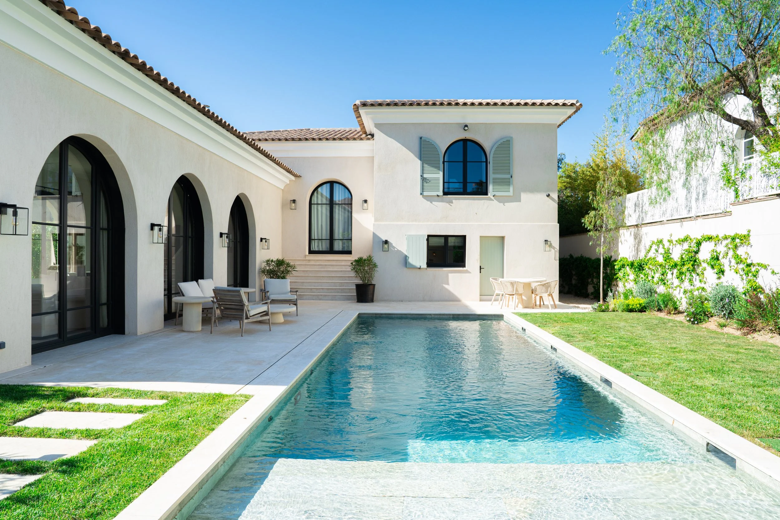 Cour arrière d'une maison avec piscine, mobilier extérieur, arbres et mur de jardin.