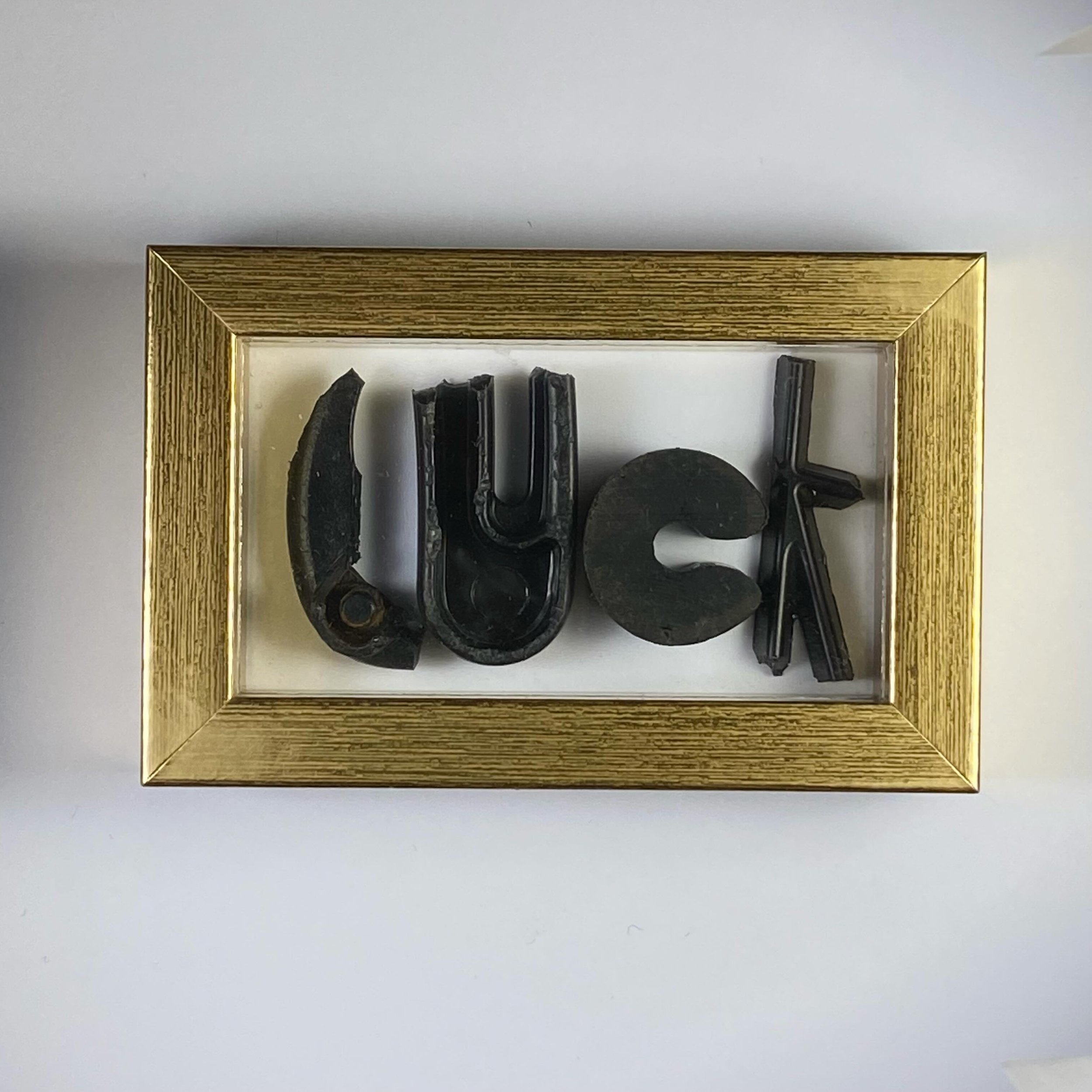 VERKOCHT Fair Werkaanhetspoel : gouden lijst (8,5cmx5,5cm) met tekst &ldquo;LUCK&rdquo; nr. (1/5) De letters zijn handgemaakt van de straat gevonden materialen. SOLD : golden frame (8,5xcm5,5cm) featuring word &ldquo;LUCK&rdquo; nr. (1/5)The letters 