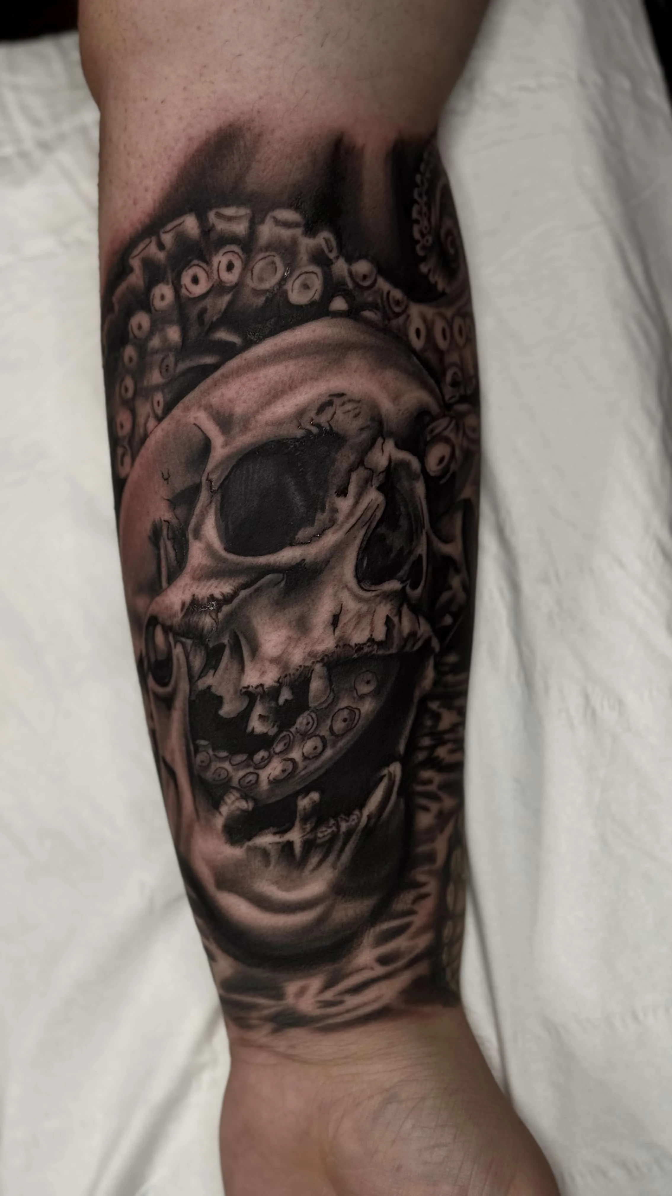 An octopus tentacle wrapping around a skull black and grey realism tattoo