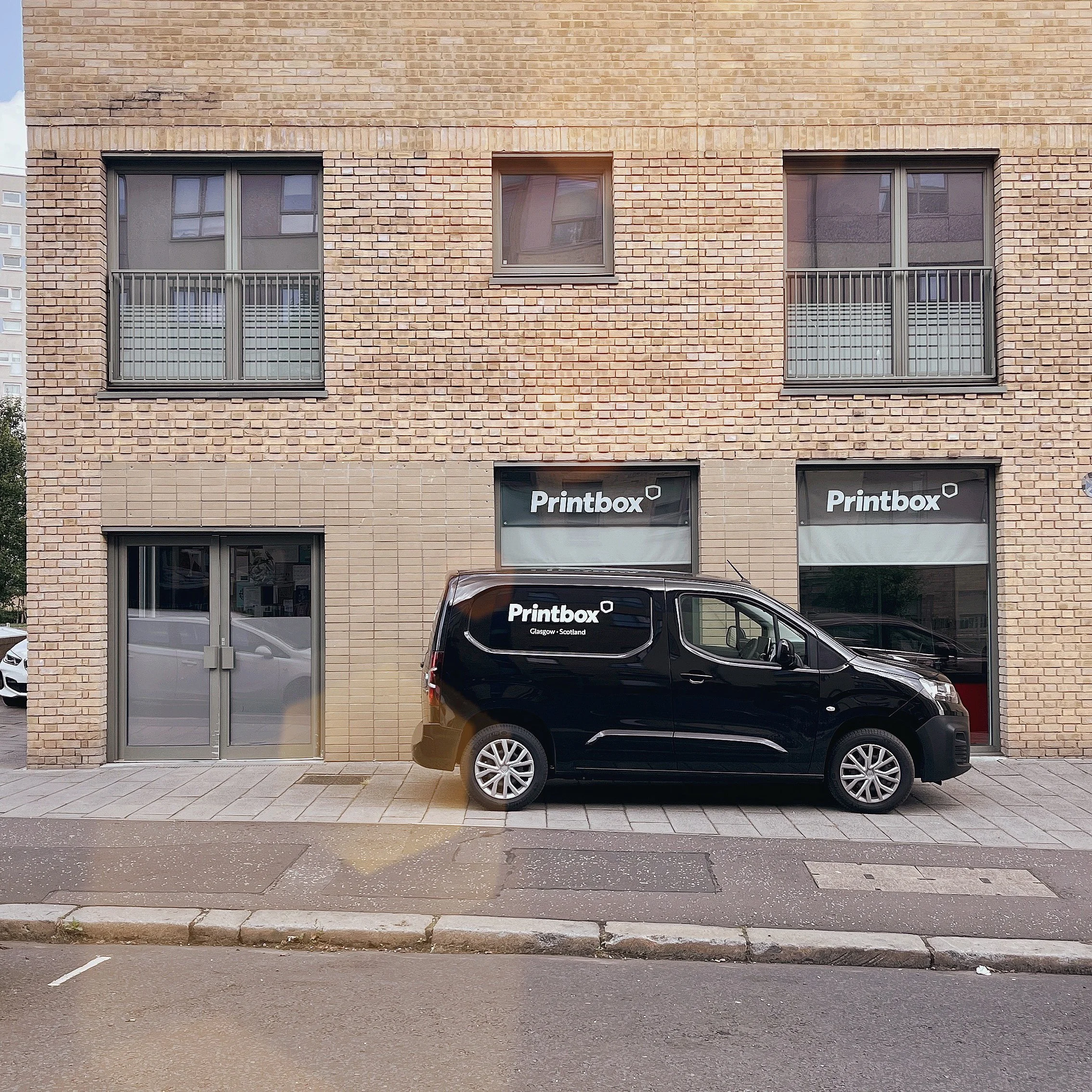 A black van parked outside a brick building with Printbox signage on the windows and door.