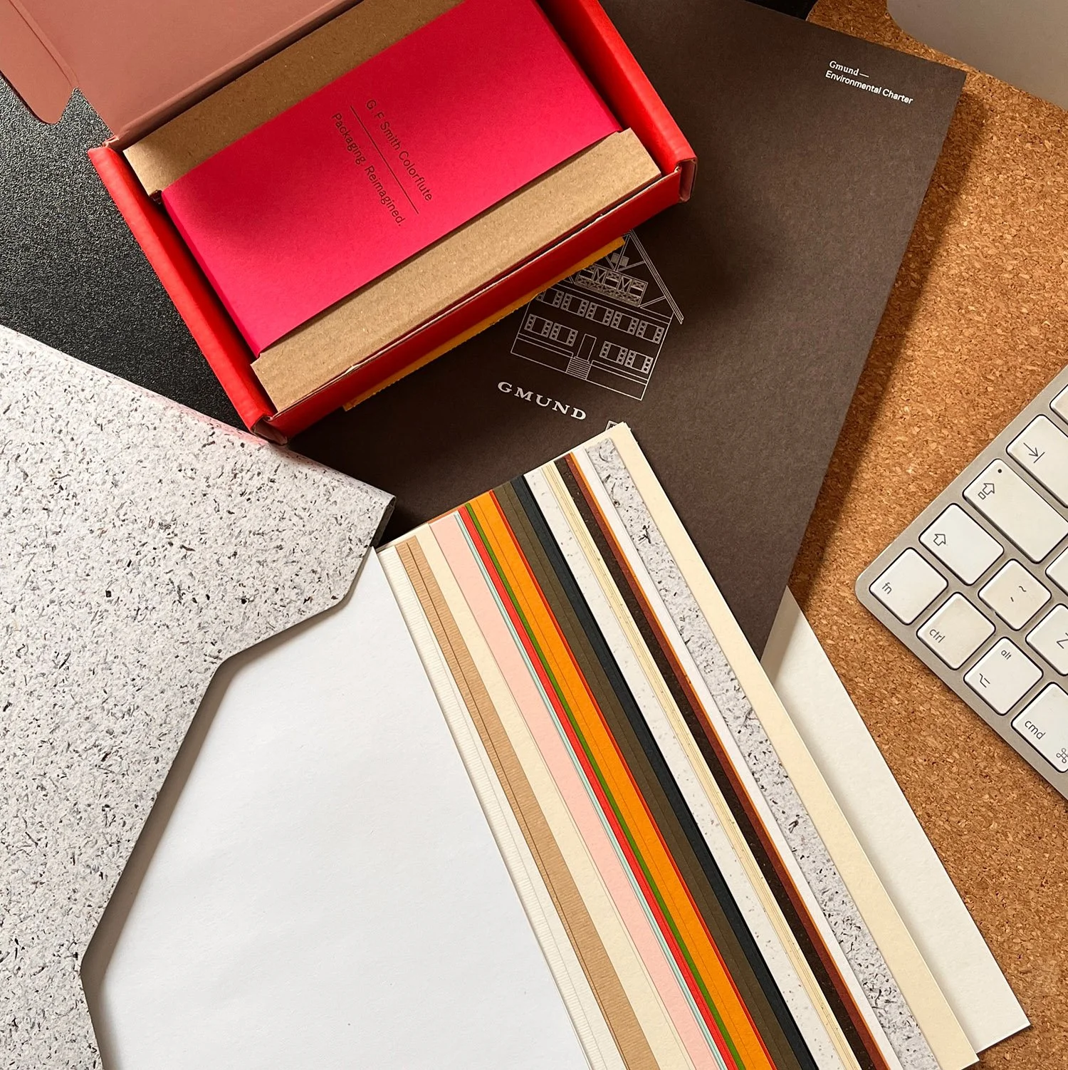 Desk with various notebooks, color swatch cards, a computer keyboard, and a corkboard surface.