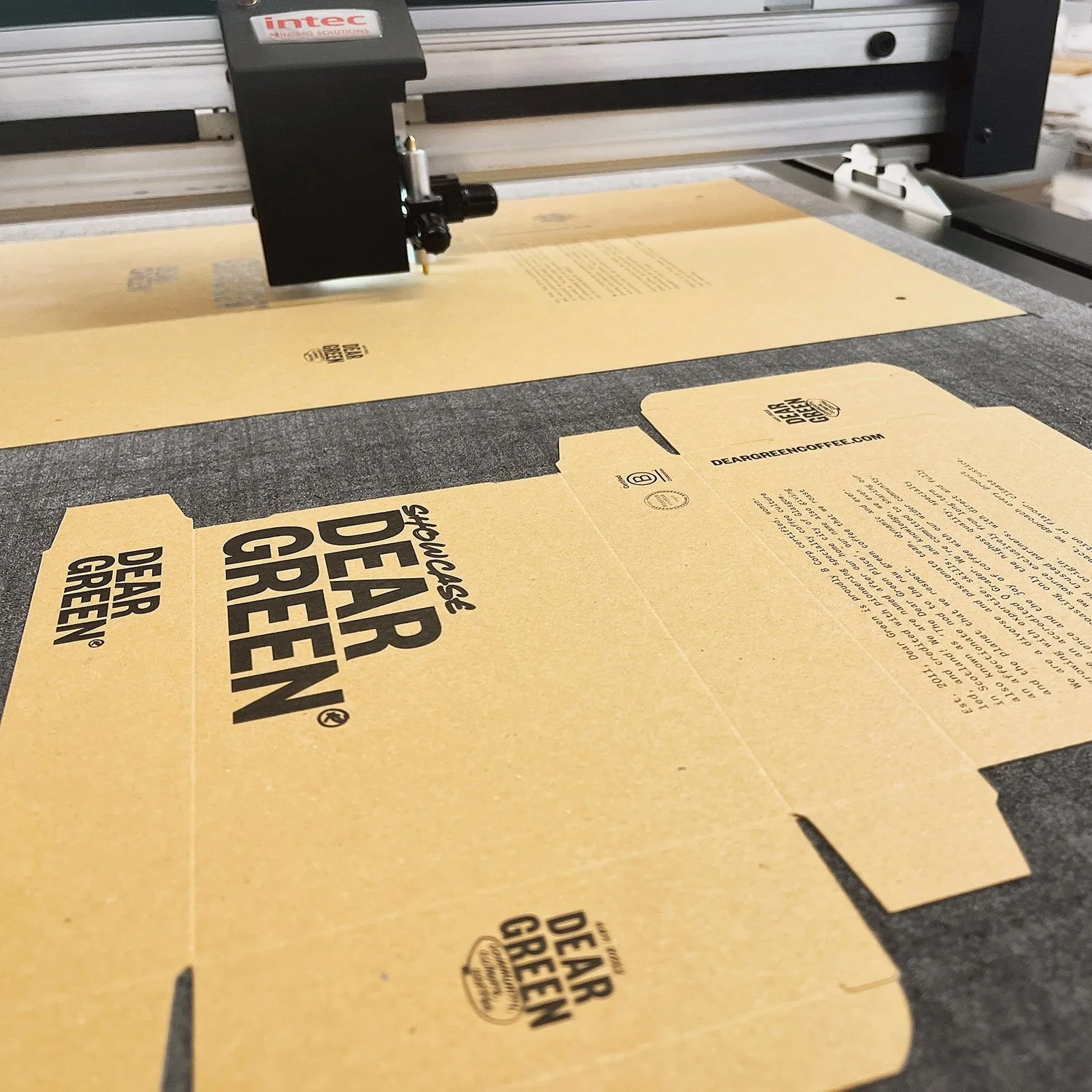 A laser cutter machine cutting a cardboard box with Dear Green Coffee branding.
