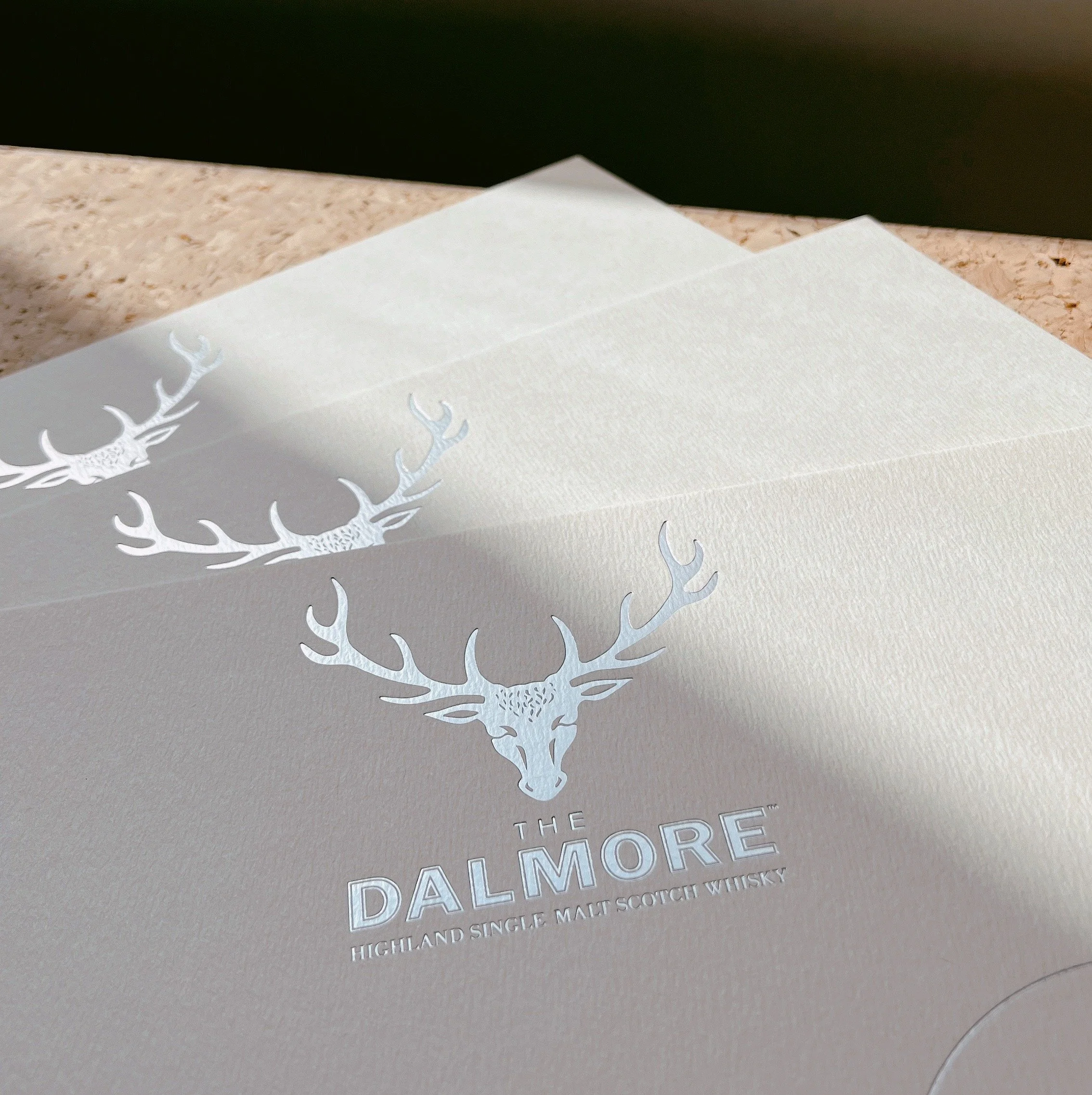 Close-up of a white sheet of paper with a silver embossed logo of a stag's head and the text 'The Dalmore Highland Single Malt Scotch Whisky'.