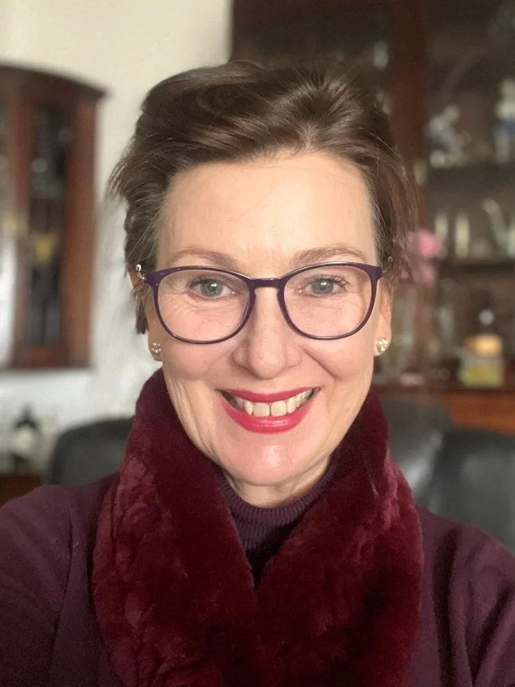 Smiling woman wearing glasses and a maroon scarf indoors.