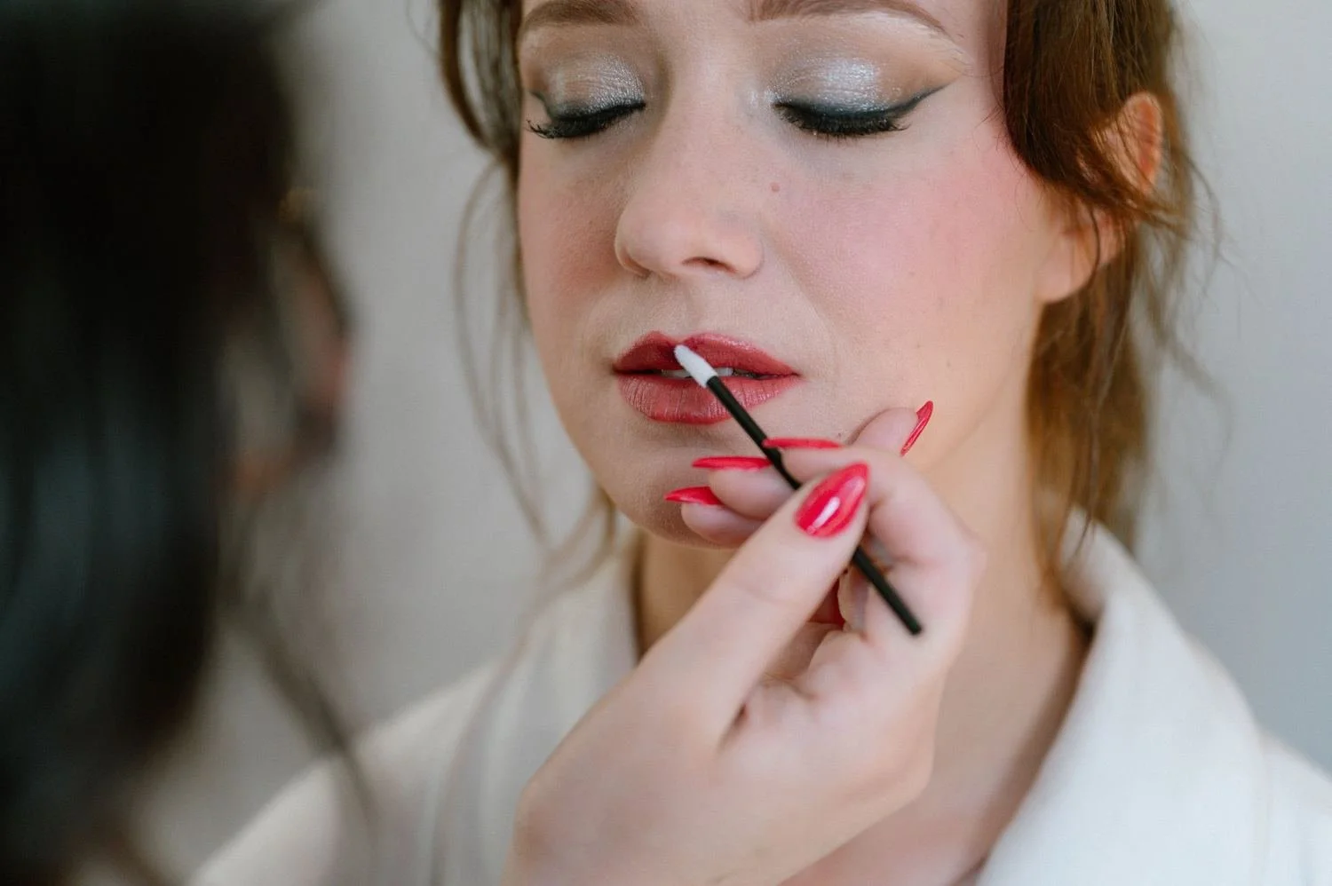 Application du rouge à lèvres au pinceau sur une mariée au teint lumineux et au regard pailleté : maquillage de mariée sur mesure