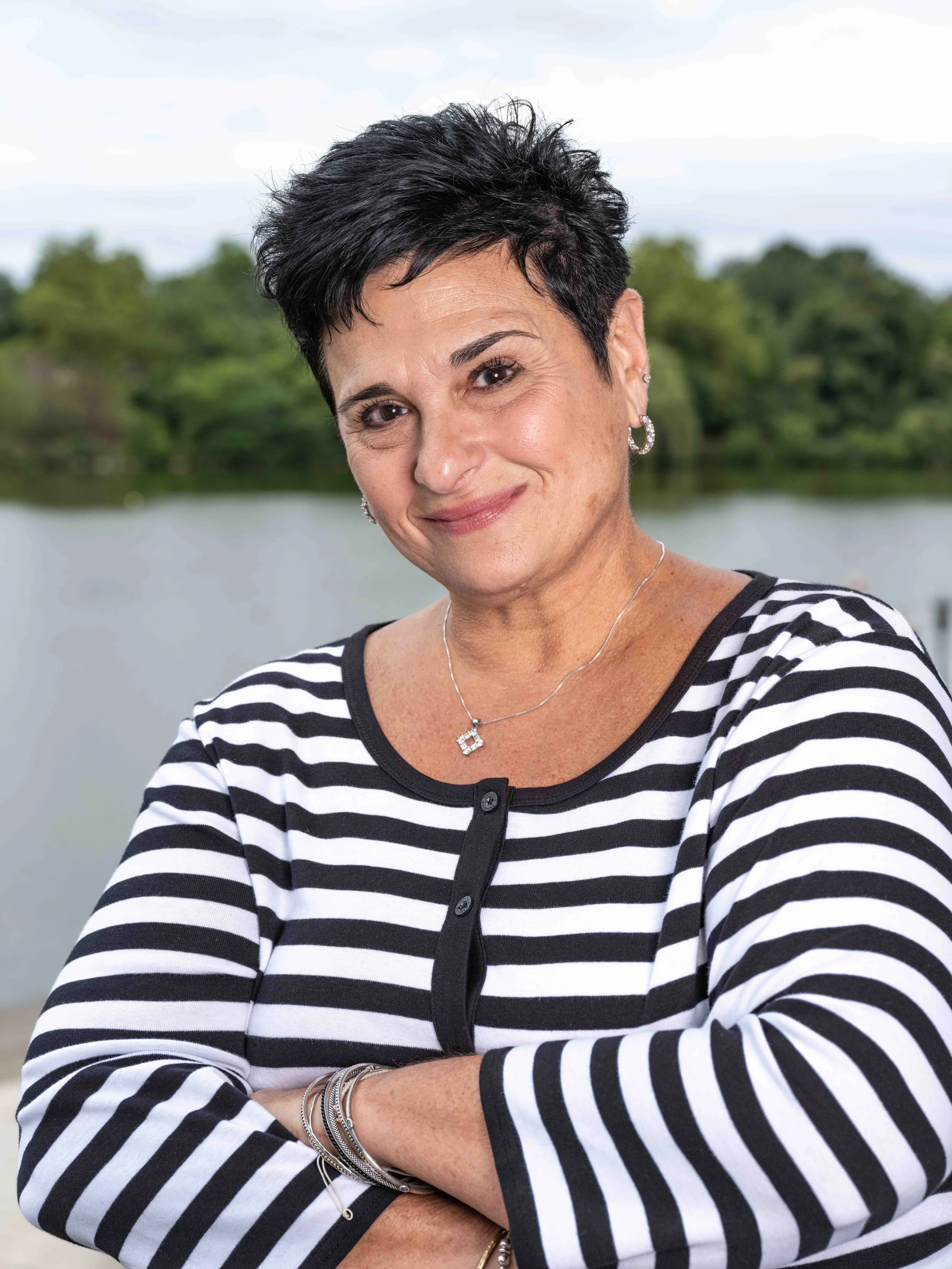 Julie Yates, Executive Administrator at Upper Edge Consulting, smiling wearing a black and white striped top, standing in front of Hoyt Lake