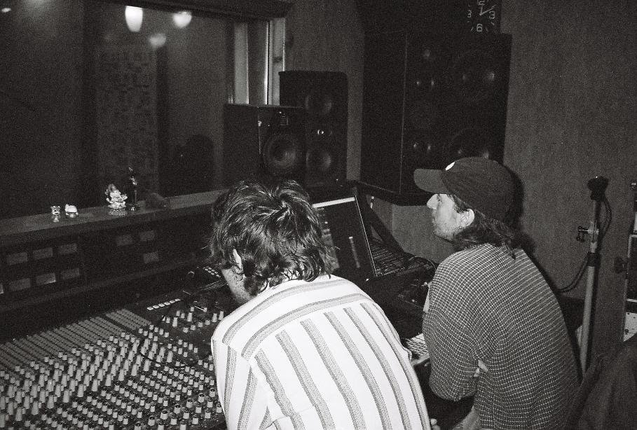 Two individuals working in a recording studio, with audio mixing equipment and speakers.