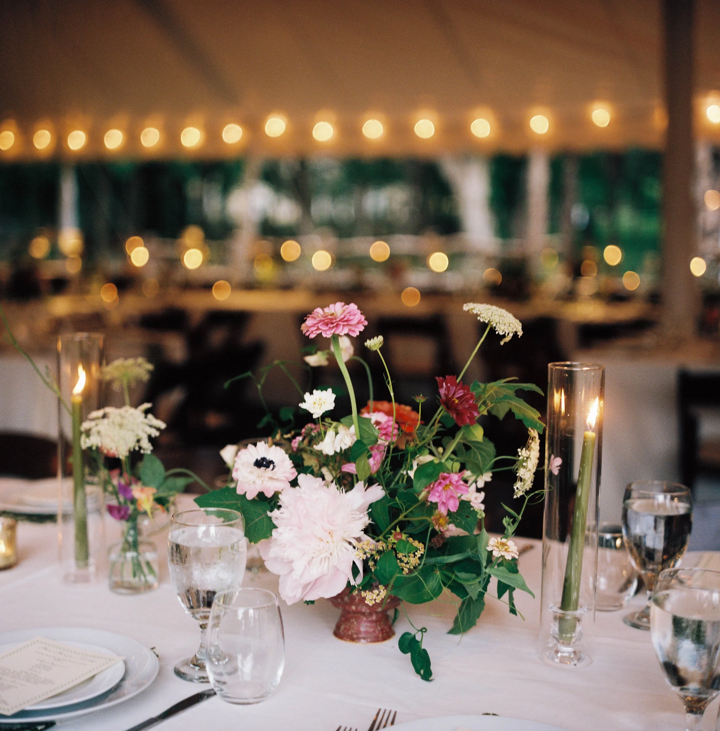 A floral centerpiece with pink, white, and red flowers in a glass vase on a decorated dining table at a formal event.