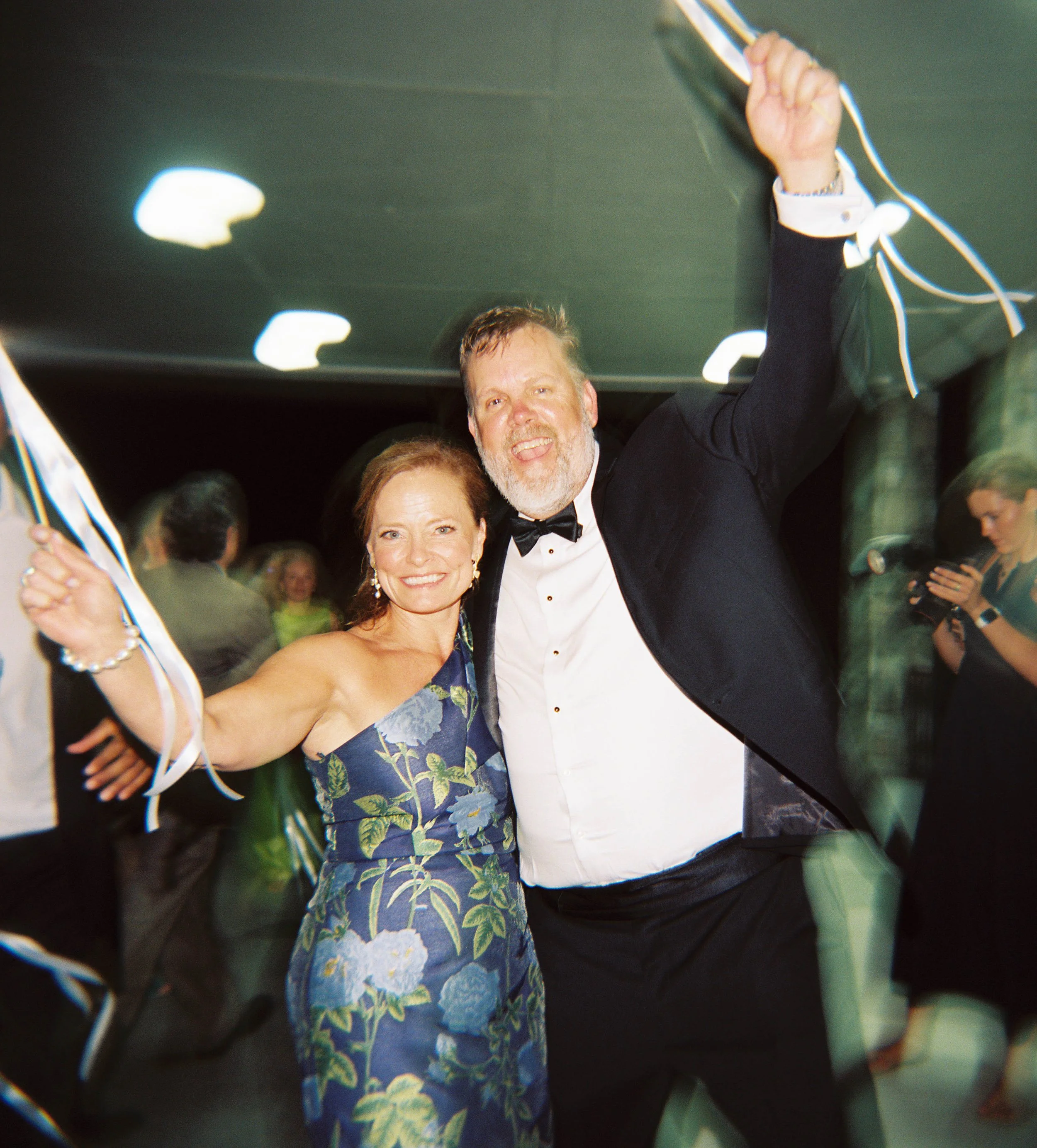 People celebrating at a formal event with one person holding a decorated bottle and smiling for the camera.