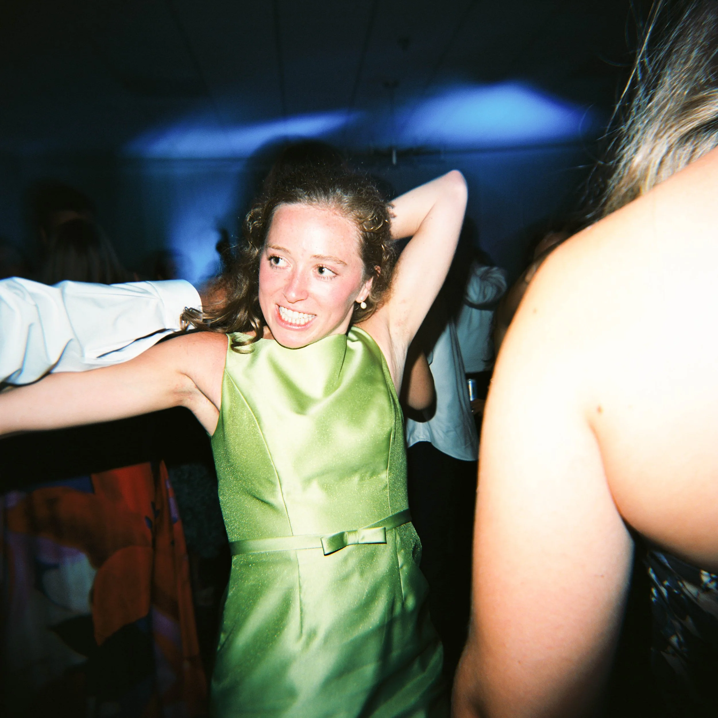 A young woman in a green dress smiling and raising her arm in a party or celebration setting.