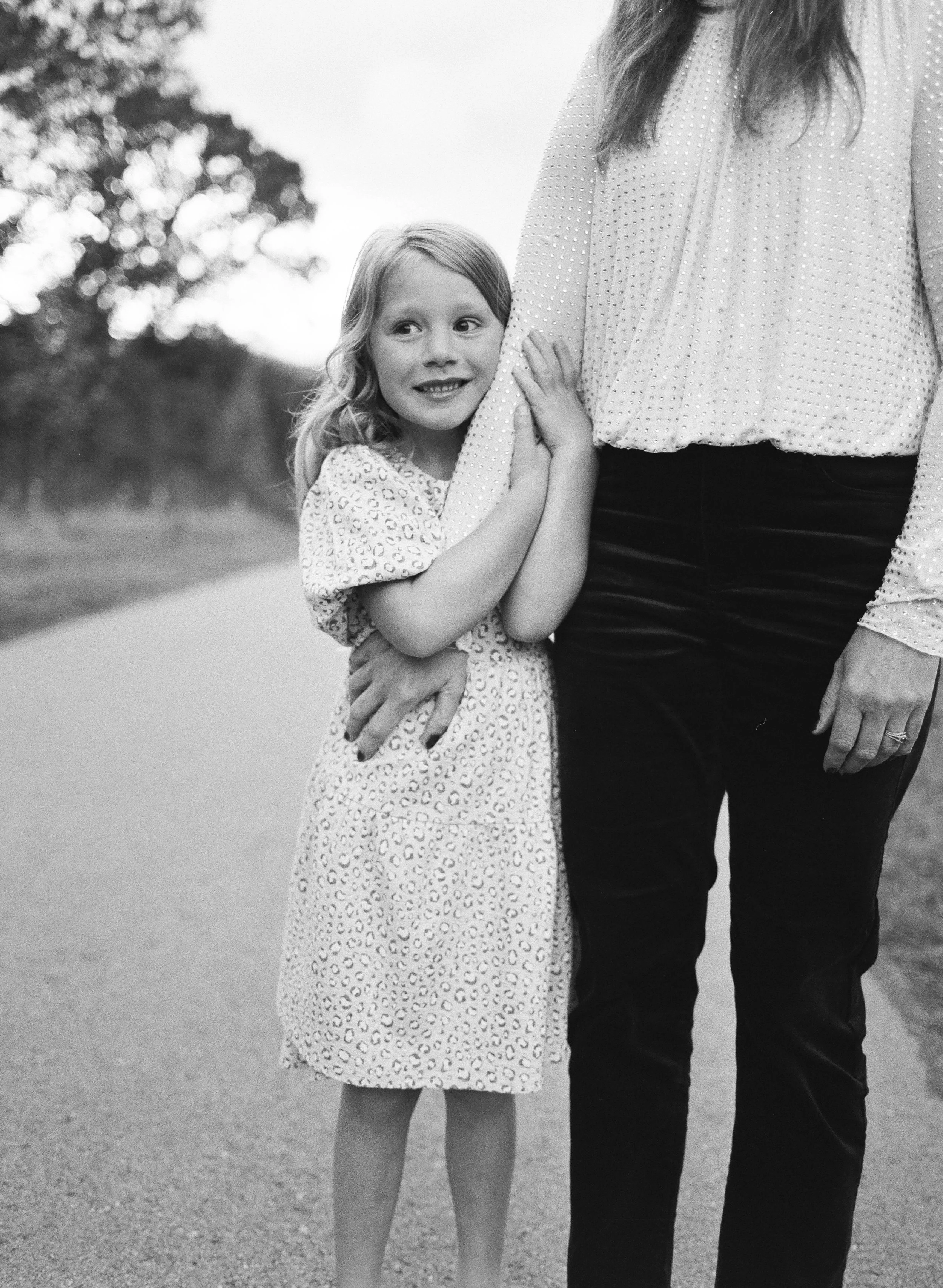 A young girl hugging an adult, partially visible, outside on a path.